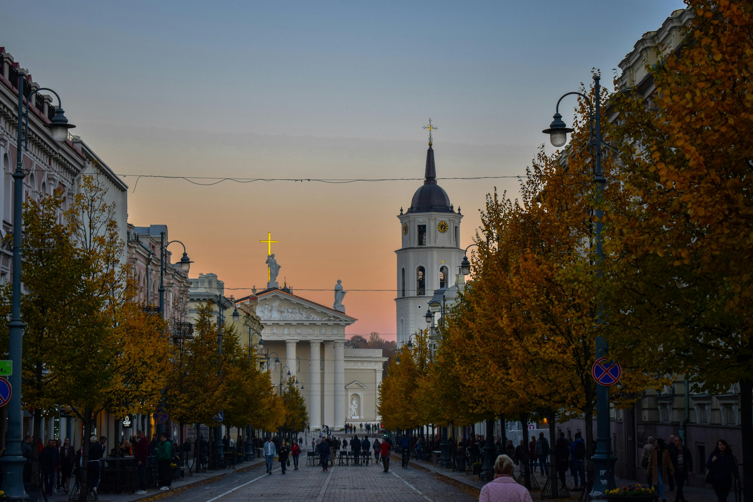 Street view of Vilnius Cathedral at sunset, featuring autumn trees lining the path and a clear sky above the historic architecture in Lithuania