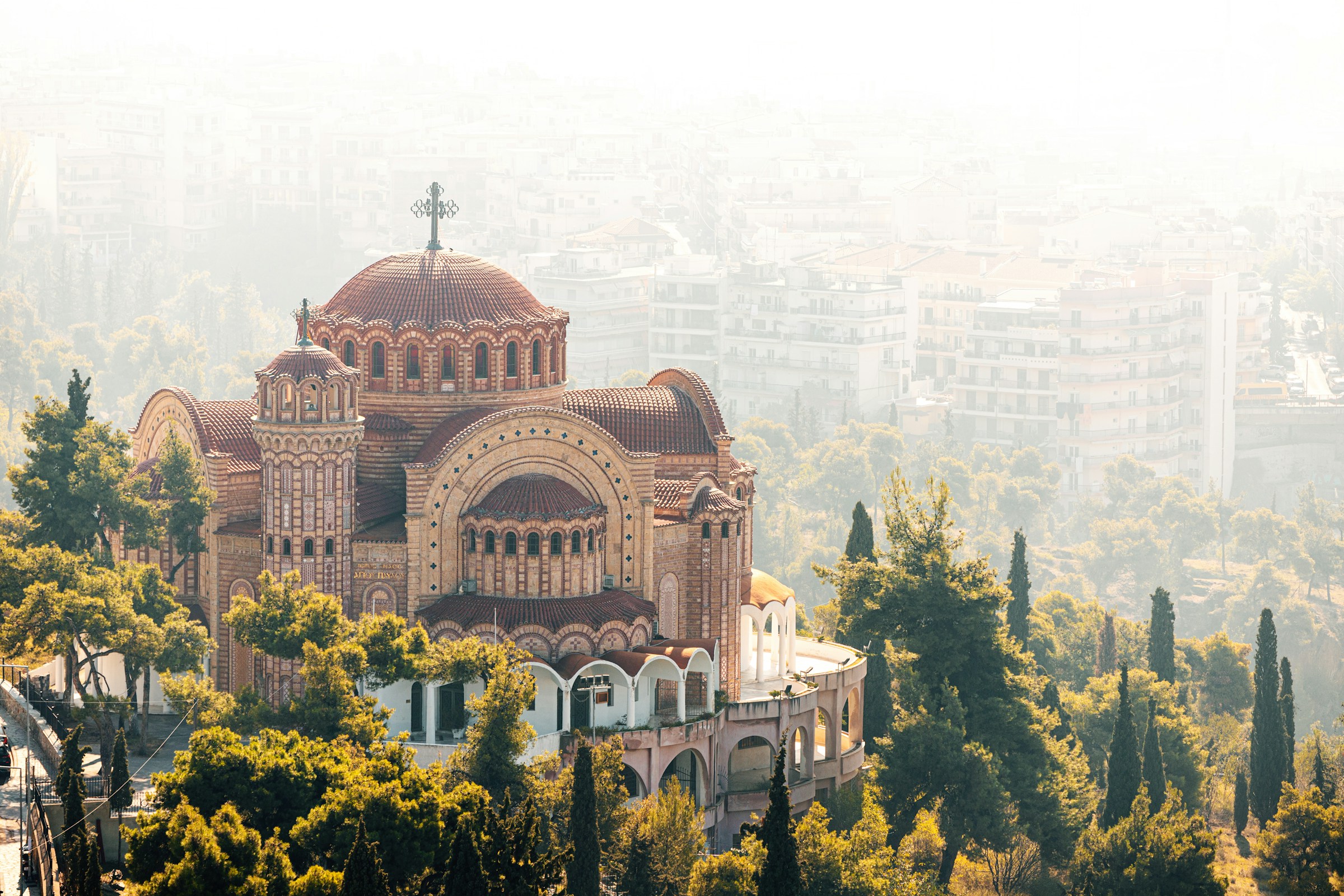Byzantine-style church with a large dome surrounded by trees, overlooking a foggy cityscape.