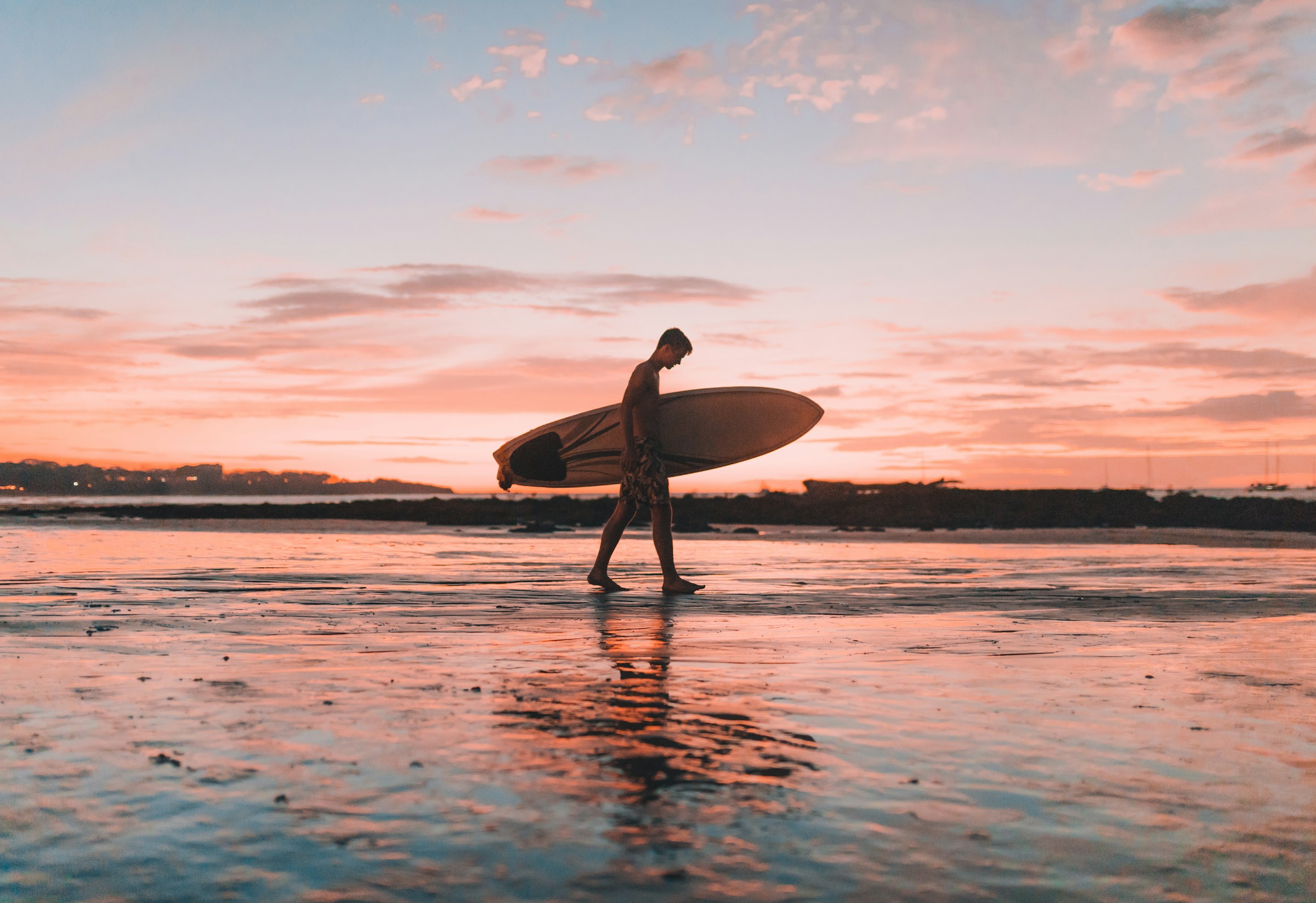 Man carrying surfboard at sunset on the beach in Costa Rica