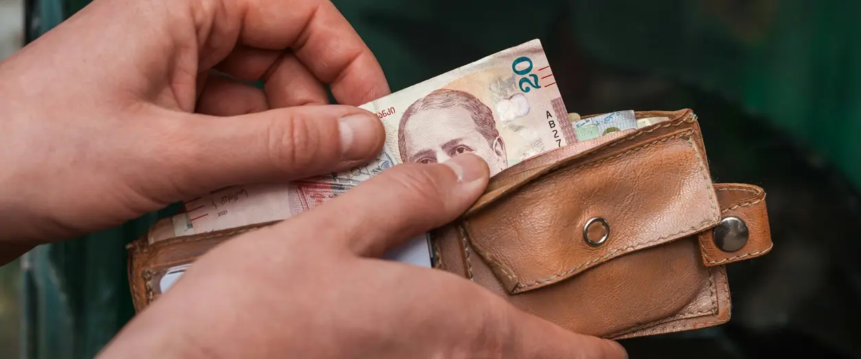 Person tar upp en sedel ur en brun pl&aring;nbok f&ouml;r att betala med kontanter.