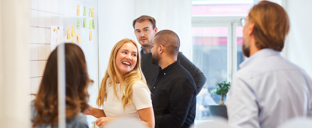 Ryhmä kollegoita seisoo kokoushuoneessa ja keskustelee