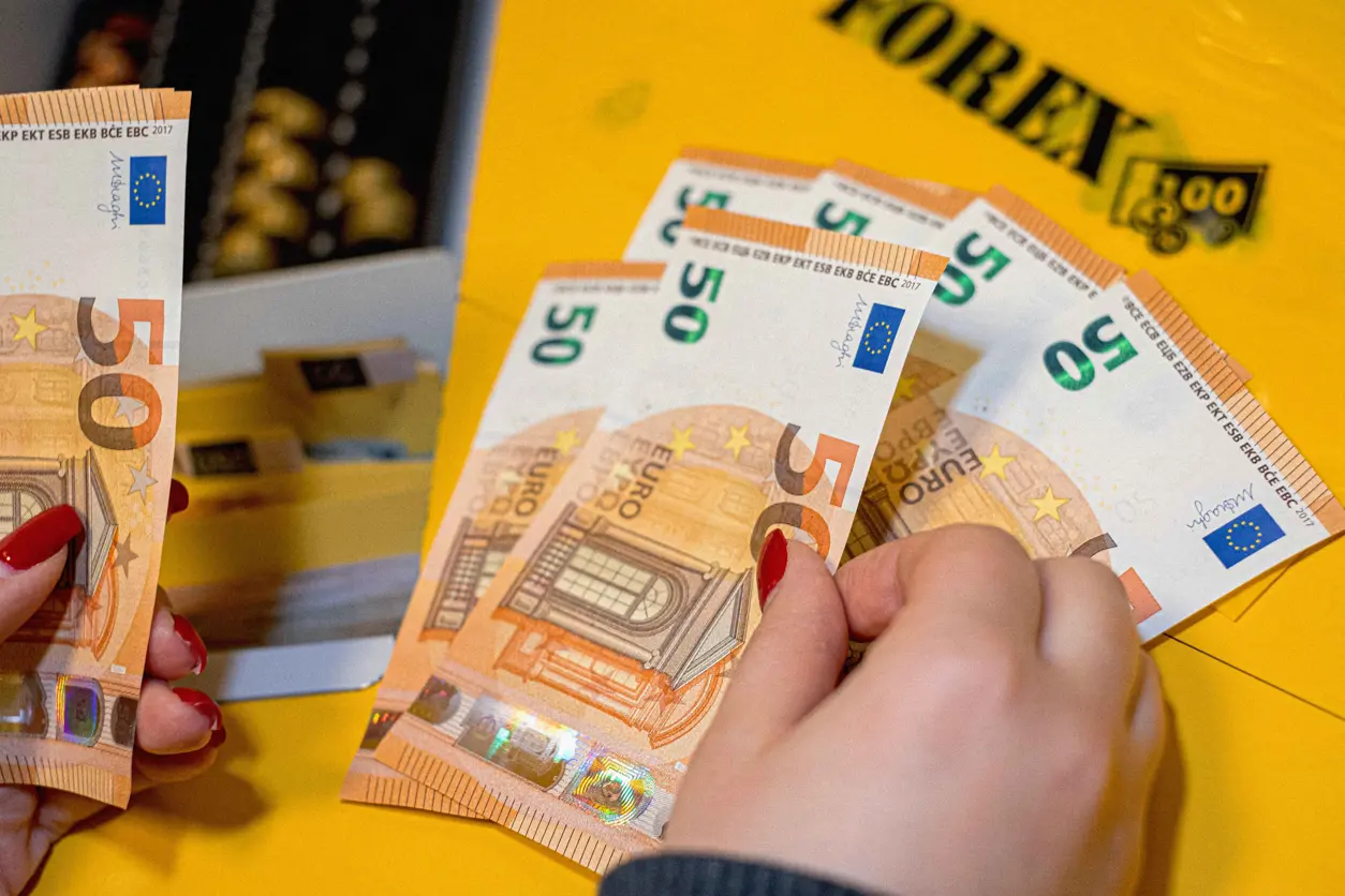 K&auml;det jakavat 50 euron seteleit&auml;, taustalla keltaisia ​​FOREX-kirjekuoria