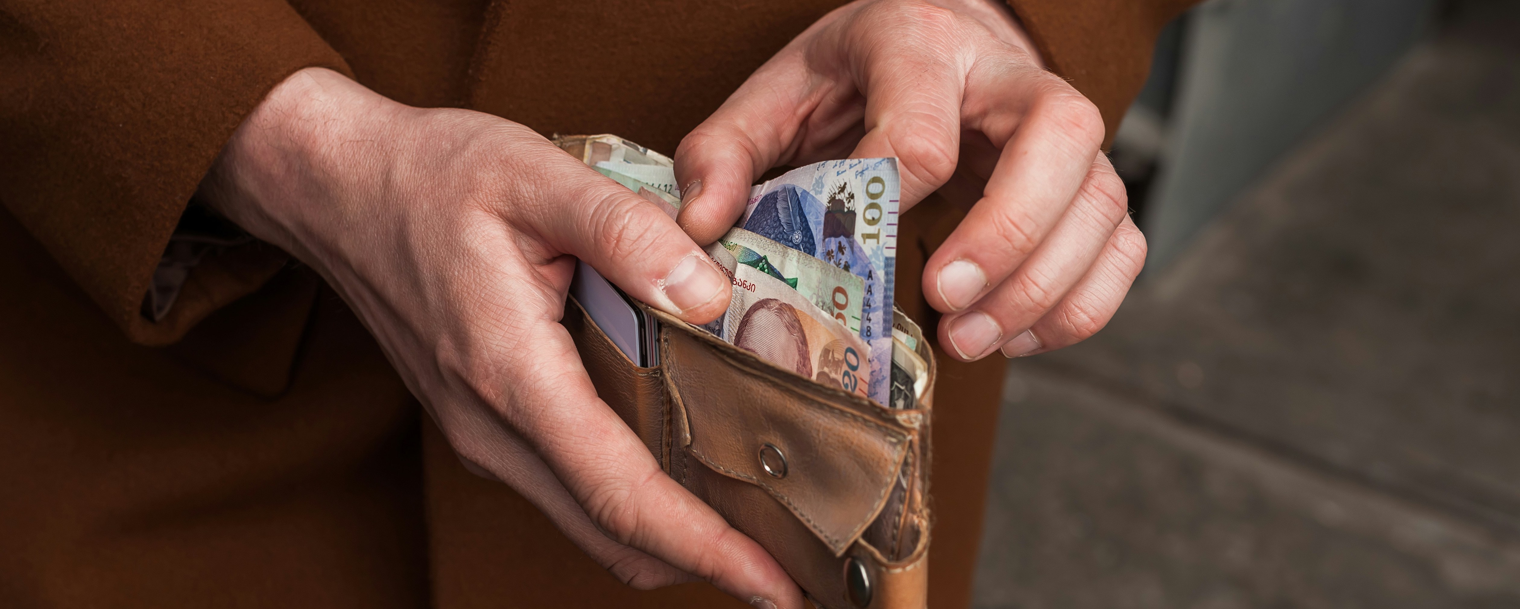 Person öppnar plånbok fylld med svenska sedlar, inklusive 500-kronorssedlar, utomhus.