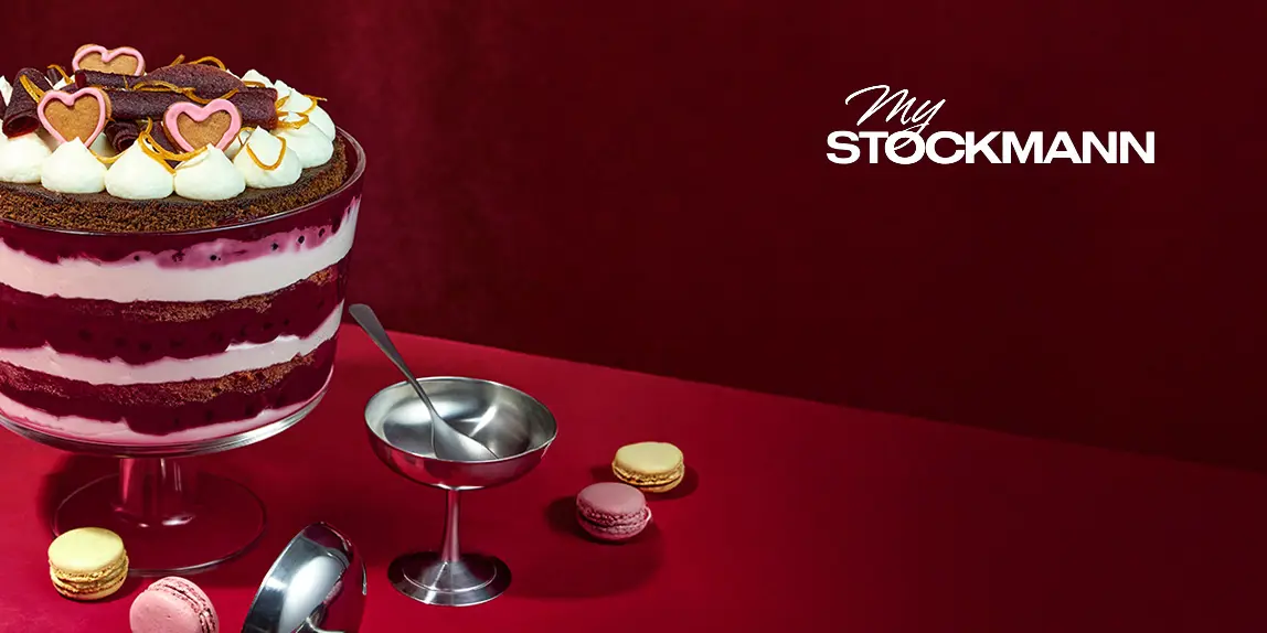 Jälkiruokamalja kerroksittain lakritsaa ja kermaa, sydänkoristeita päällä, punaisella pöydällä macarons-leivosten kanssa, vieressä pieni kastikekulho. Taustalla My Stockmann -logo.