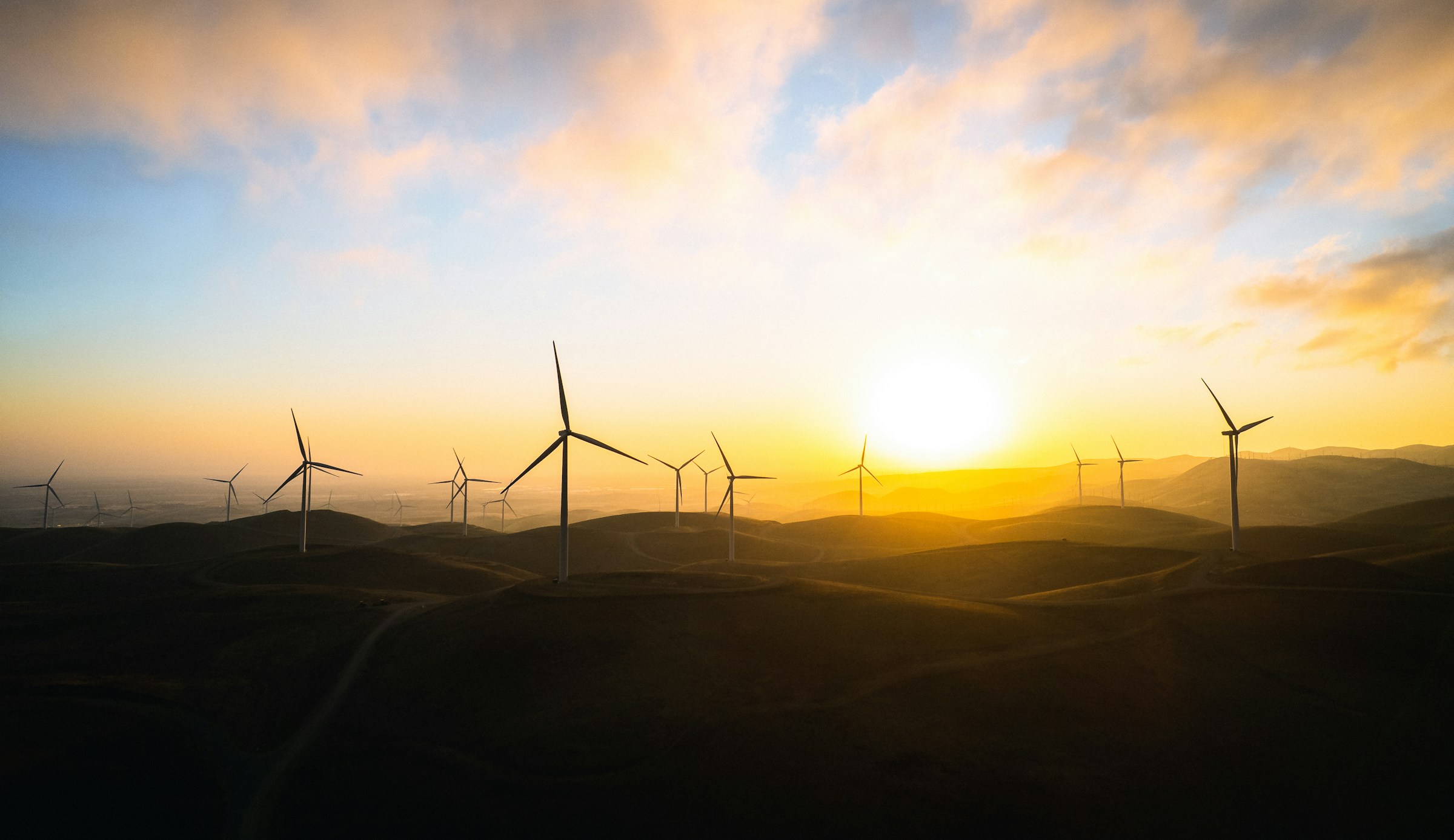 Tuuliturbiineja kukkulalla auringonlaskun aikaan maalauksellisella taivaalla