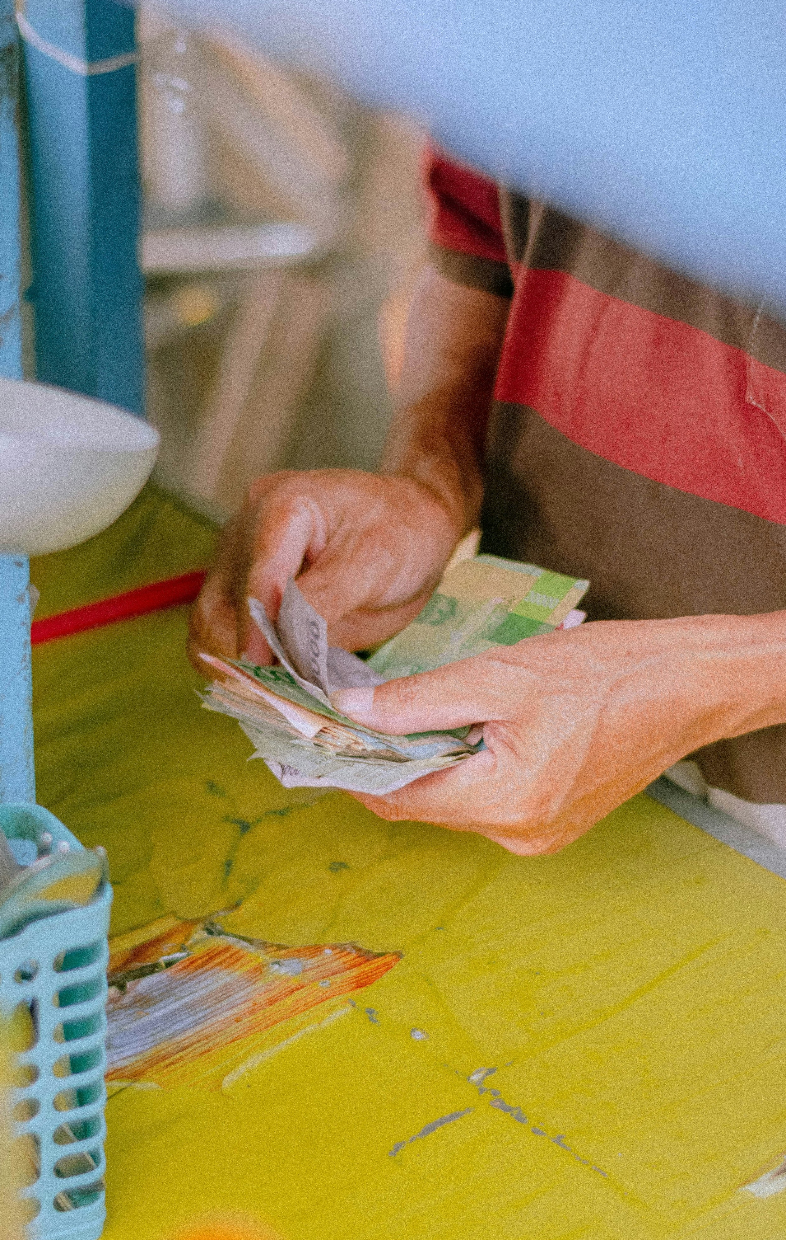 Person räknar kontanter vid ett färgglatt matstånd, omgiven av bestick, såser och köksutrustning.