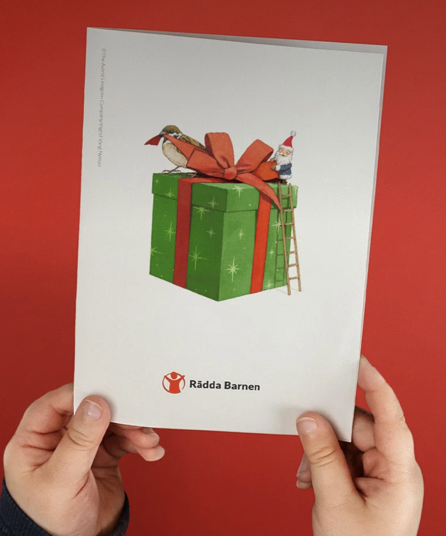 Two hands holding a Save the Children brochure with a Christmas present on it against a red background