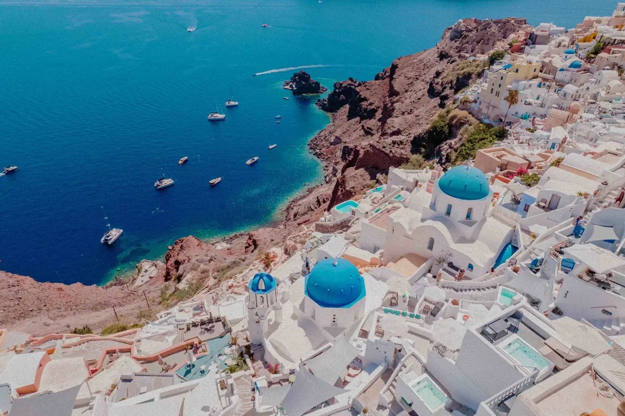 Panoramautsikt &ouml;ver Santorini med vita byggnader, bl&aring; kupoler och kristallklart hav. Ikonisk grekisk &ouml; i Kykladerna.