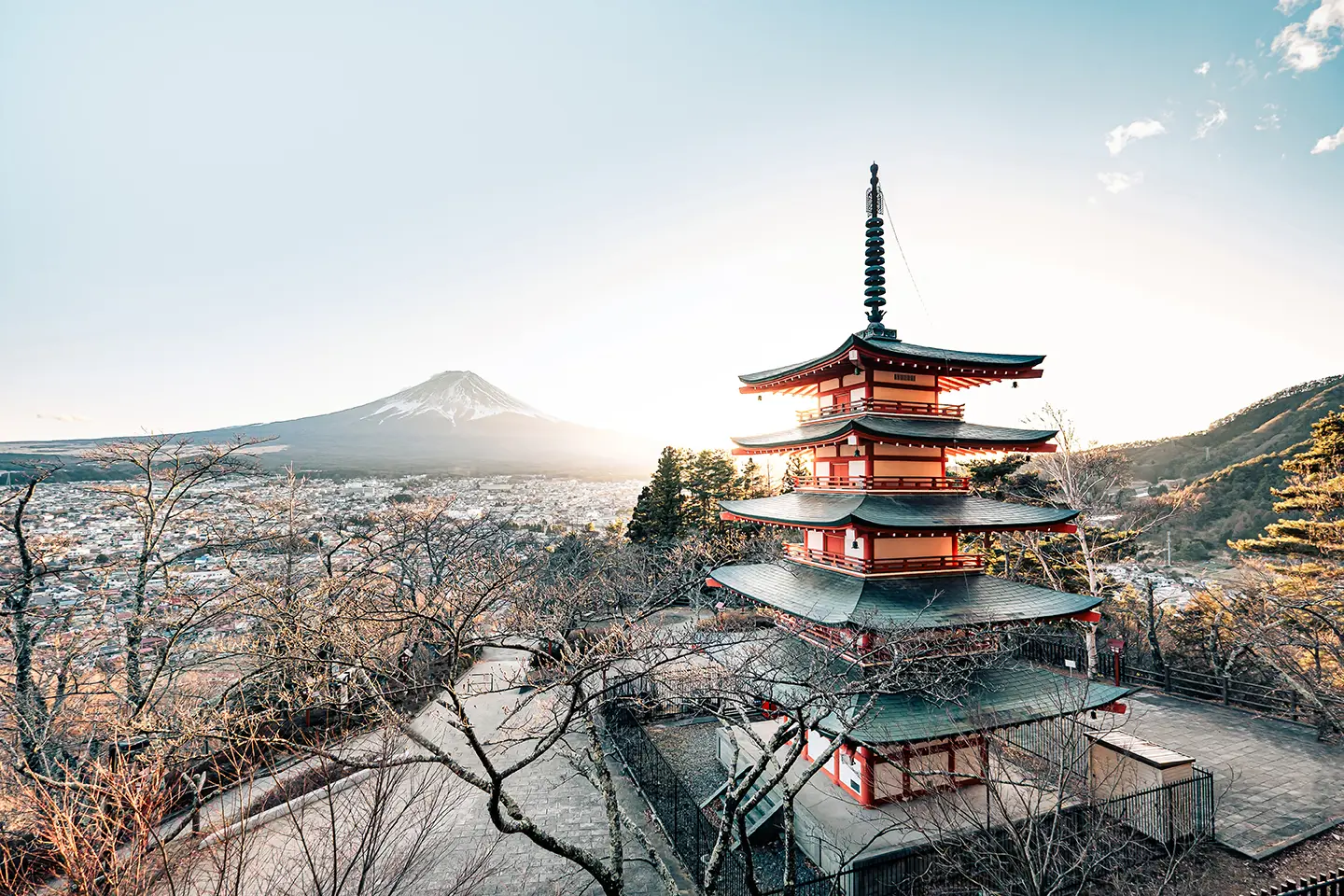 Pagod med fem våningar i Japan med soluppgång över Fuji-berget i bakgrunden, omgiven av träd och ett stadscape.