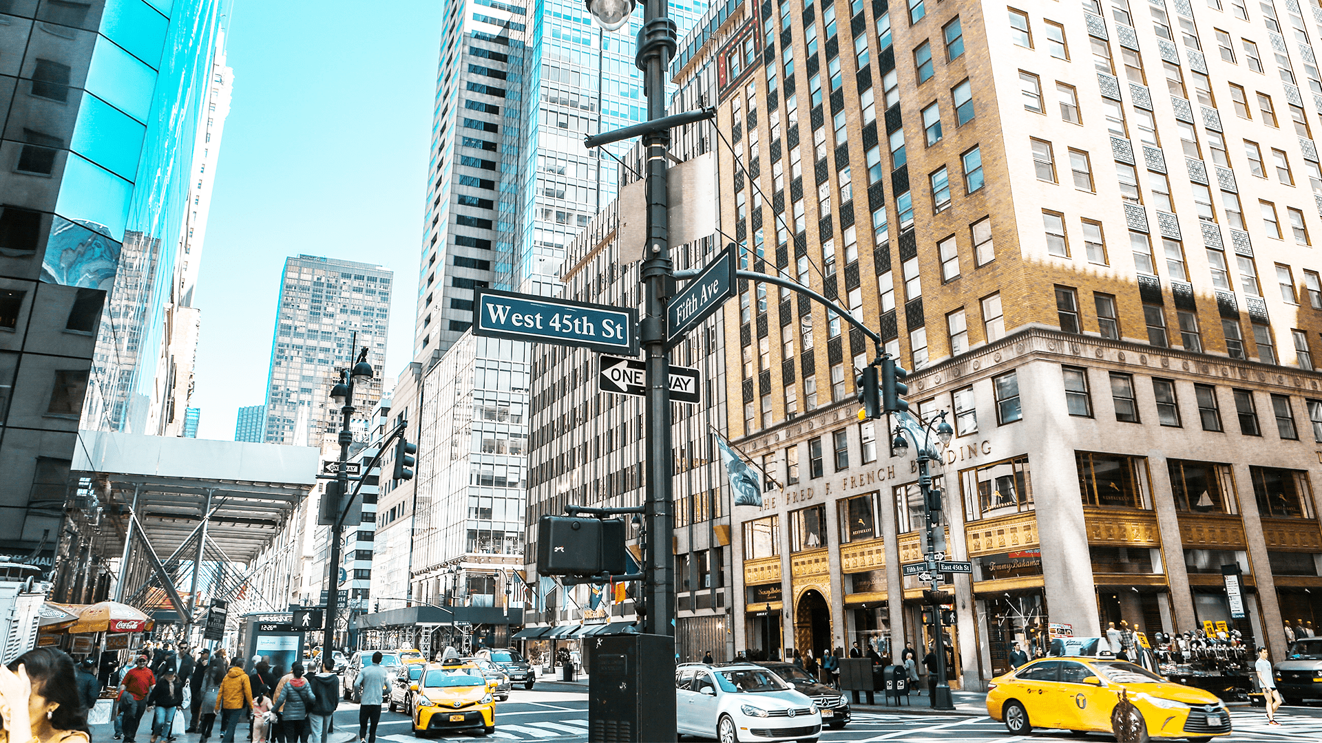 Korsningen mellan Fifth Avenue och West 45th Street i New York City med höga byggnader, livliga fotgängare och gula taxibilar i förgrunden.