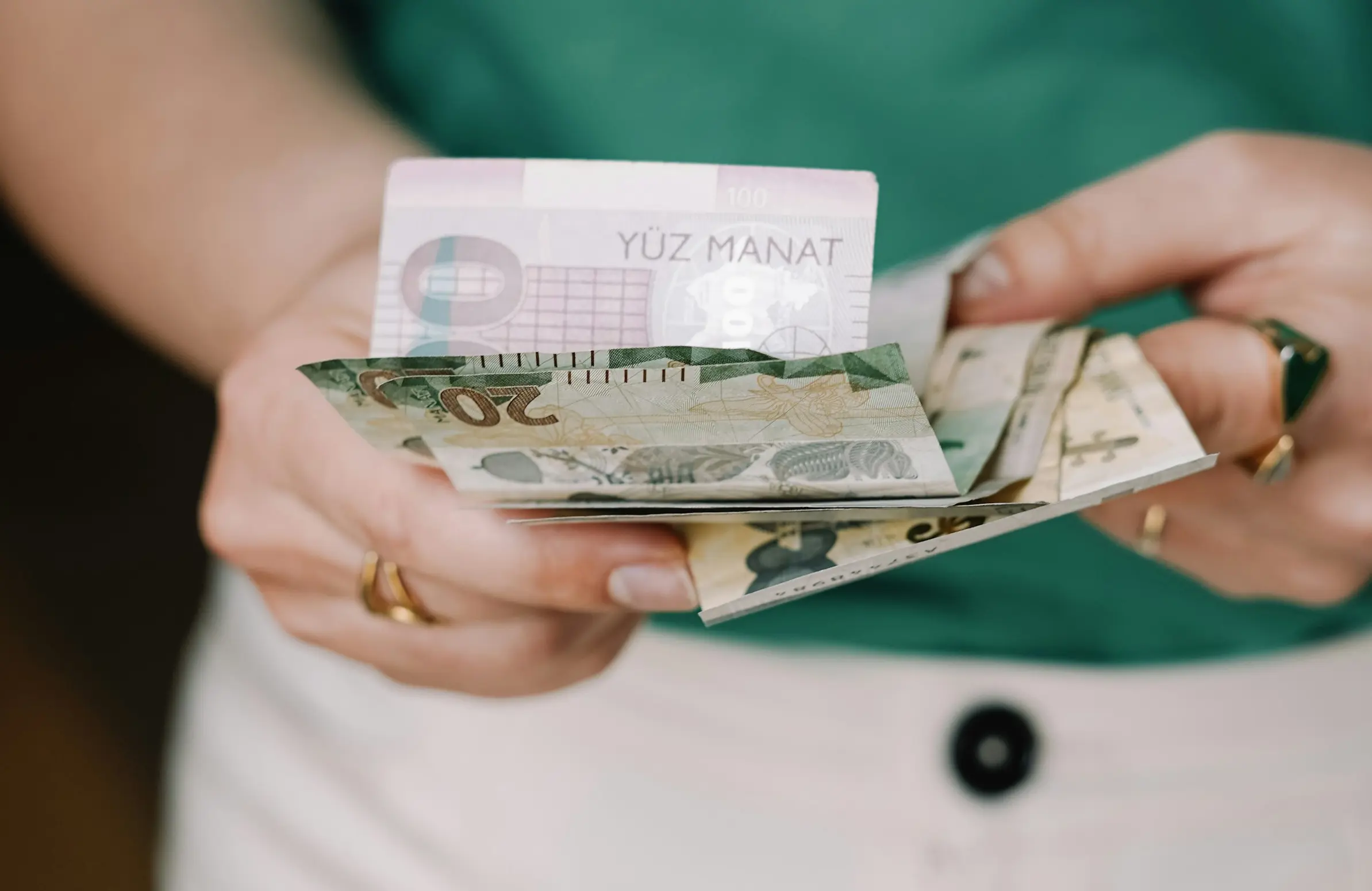 Focused close-up of cash in a woman's hands with a green sweater and white pants in the background