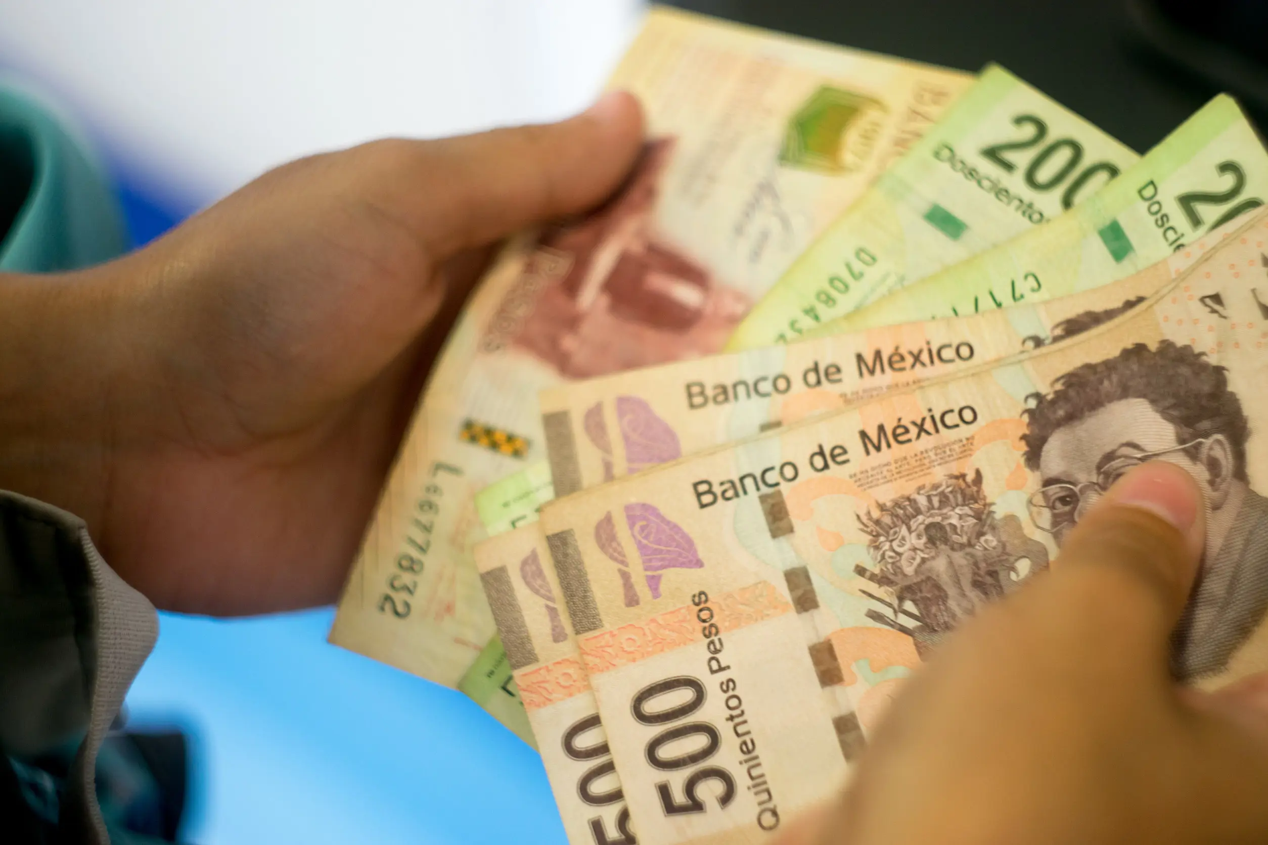 Person håller mexikanska pesos i olika valörer, inklusive 500- och 200-sedlar, med texten "Banco de México".
