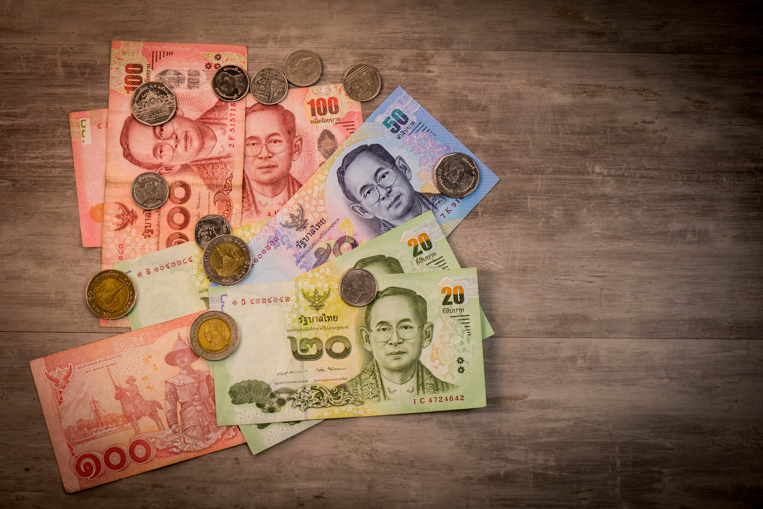 Thaimaan bahtin setelit ja kolikot hajallaan puulattialla.