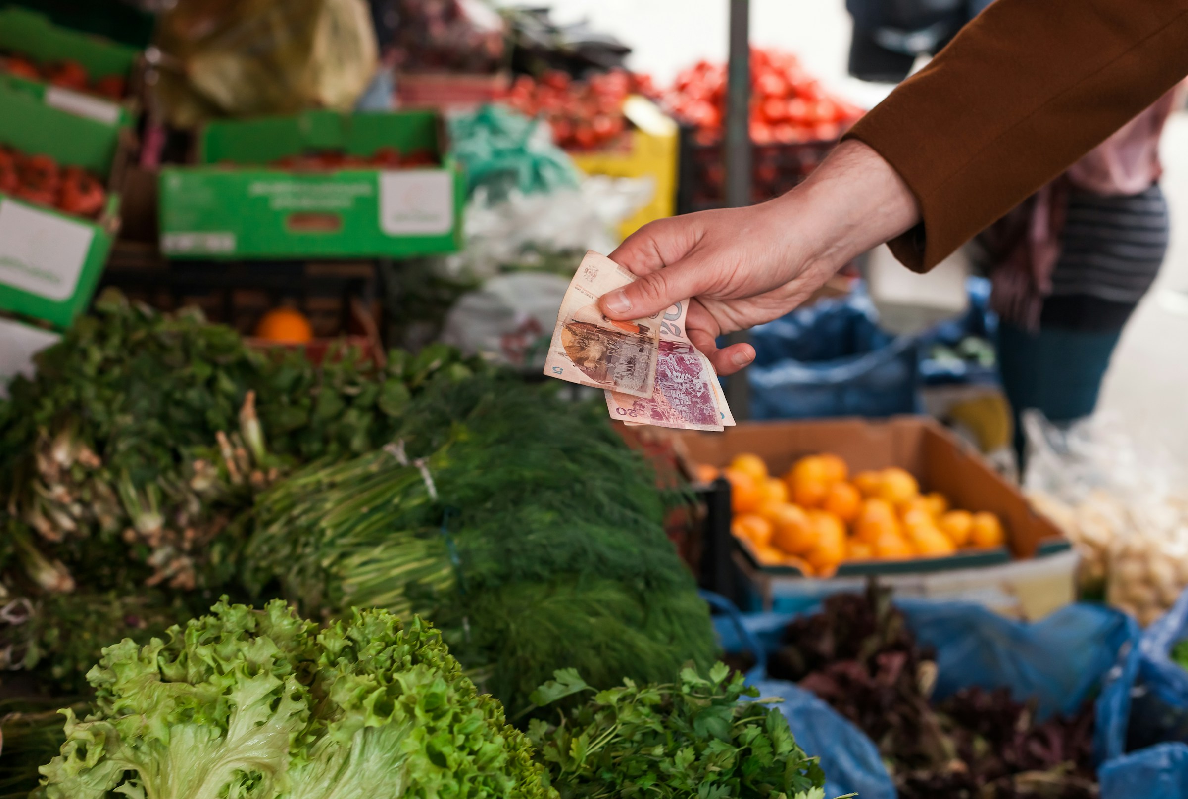 Henkilö ostaa vihanneksia ulkotorilta ja pitää rahaa tuoreista salaatinpäistä ja muista vihanneksista Ruotsissa.