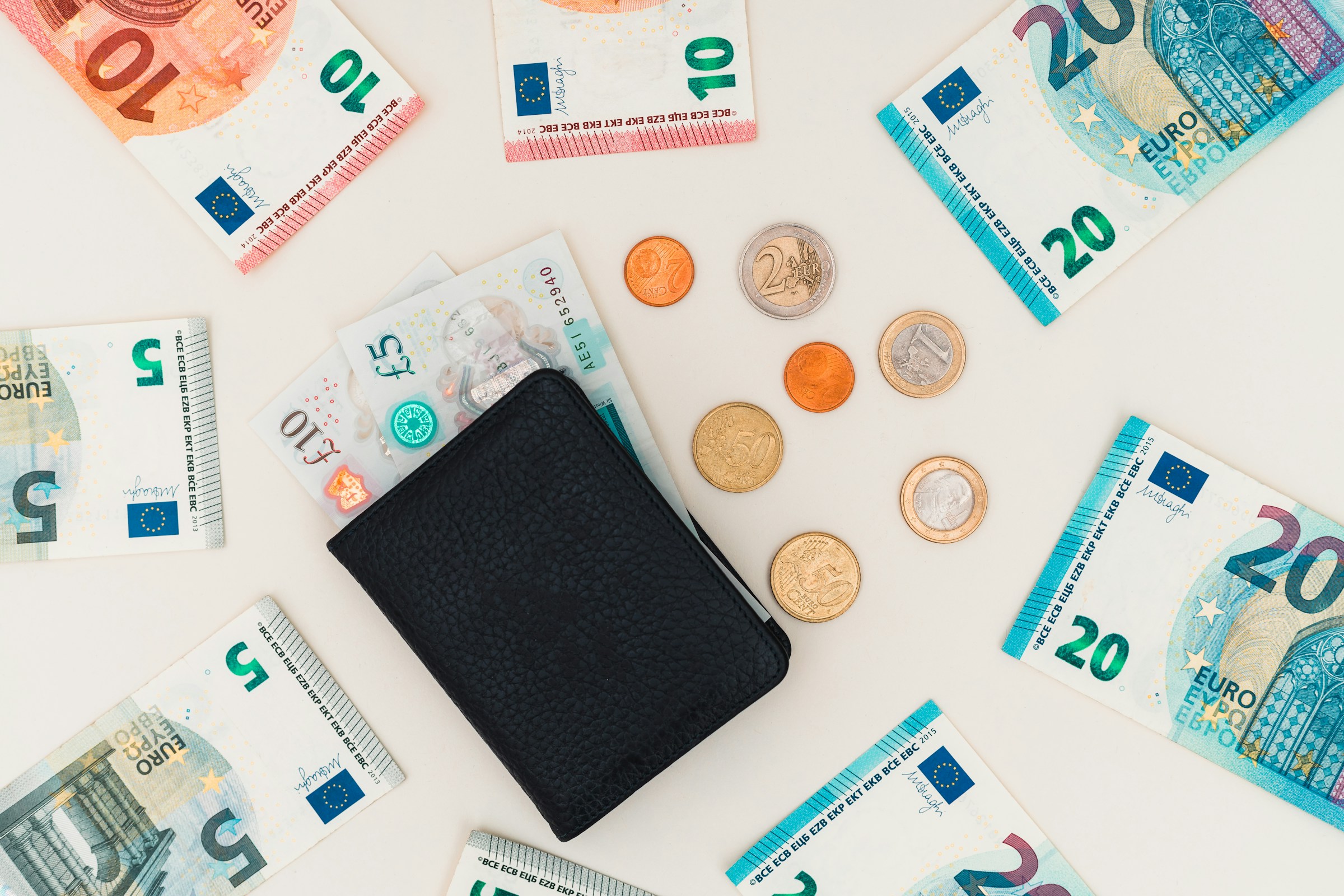 Black wallet surrounded by euro banknotes and coins on a light background, symbolizing financial planning and currency management.