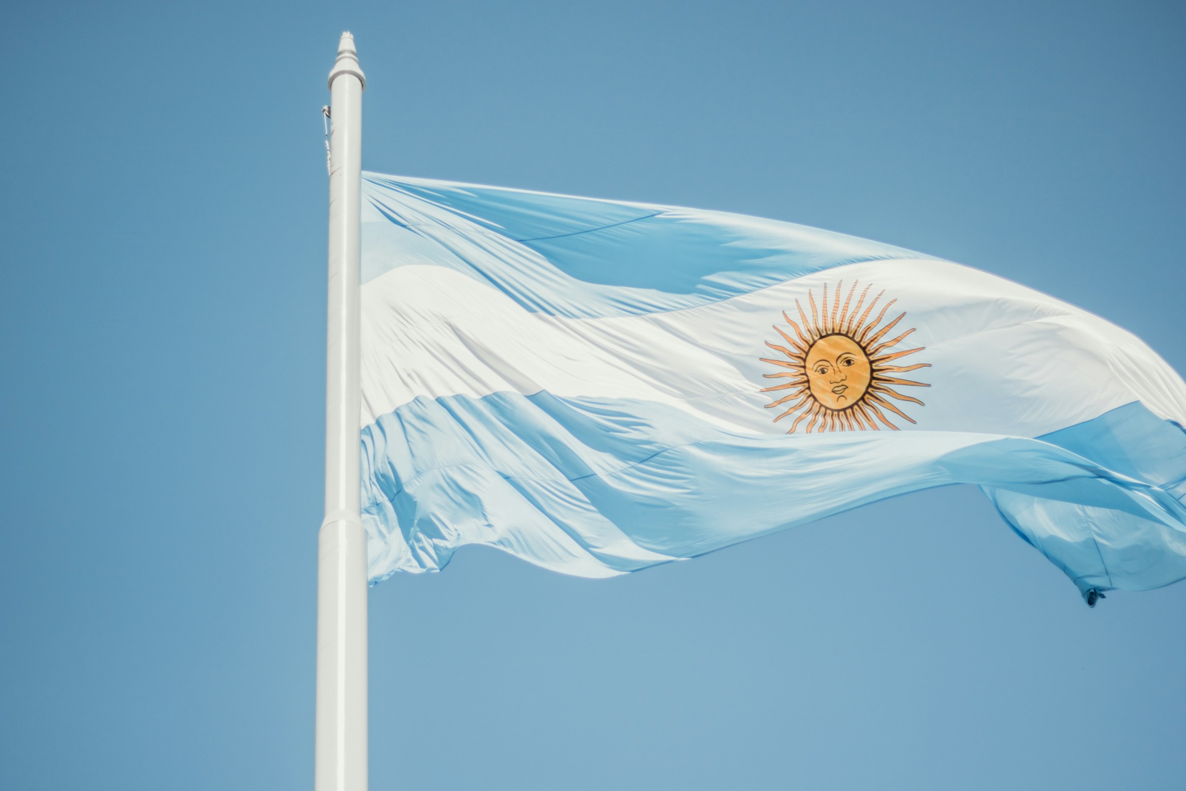 Argentinian flag with sun emblem waving against a clear blue sky.