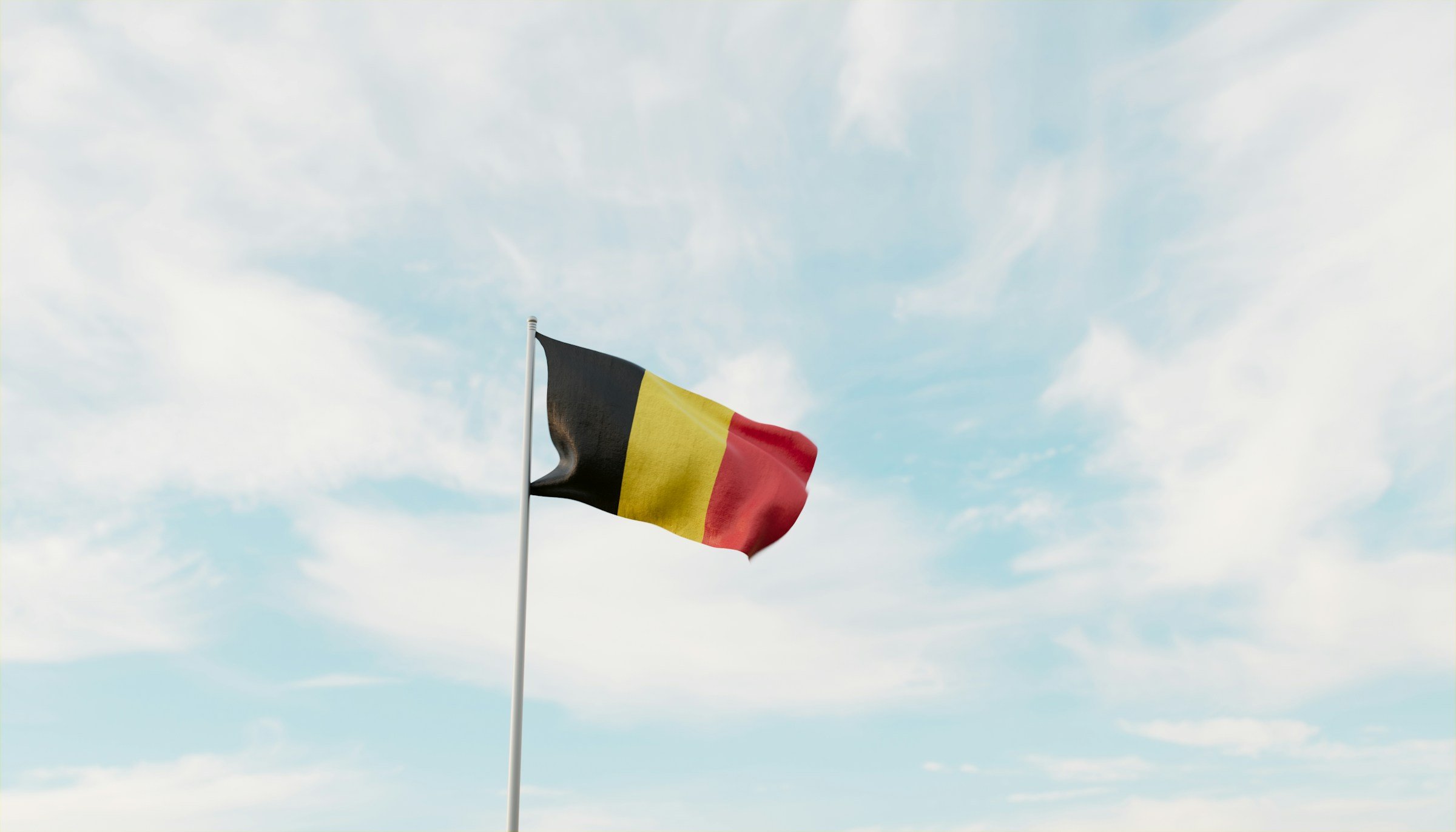 Belgium flag waving against a blue sky with clouds.