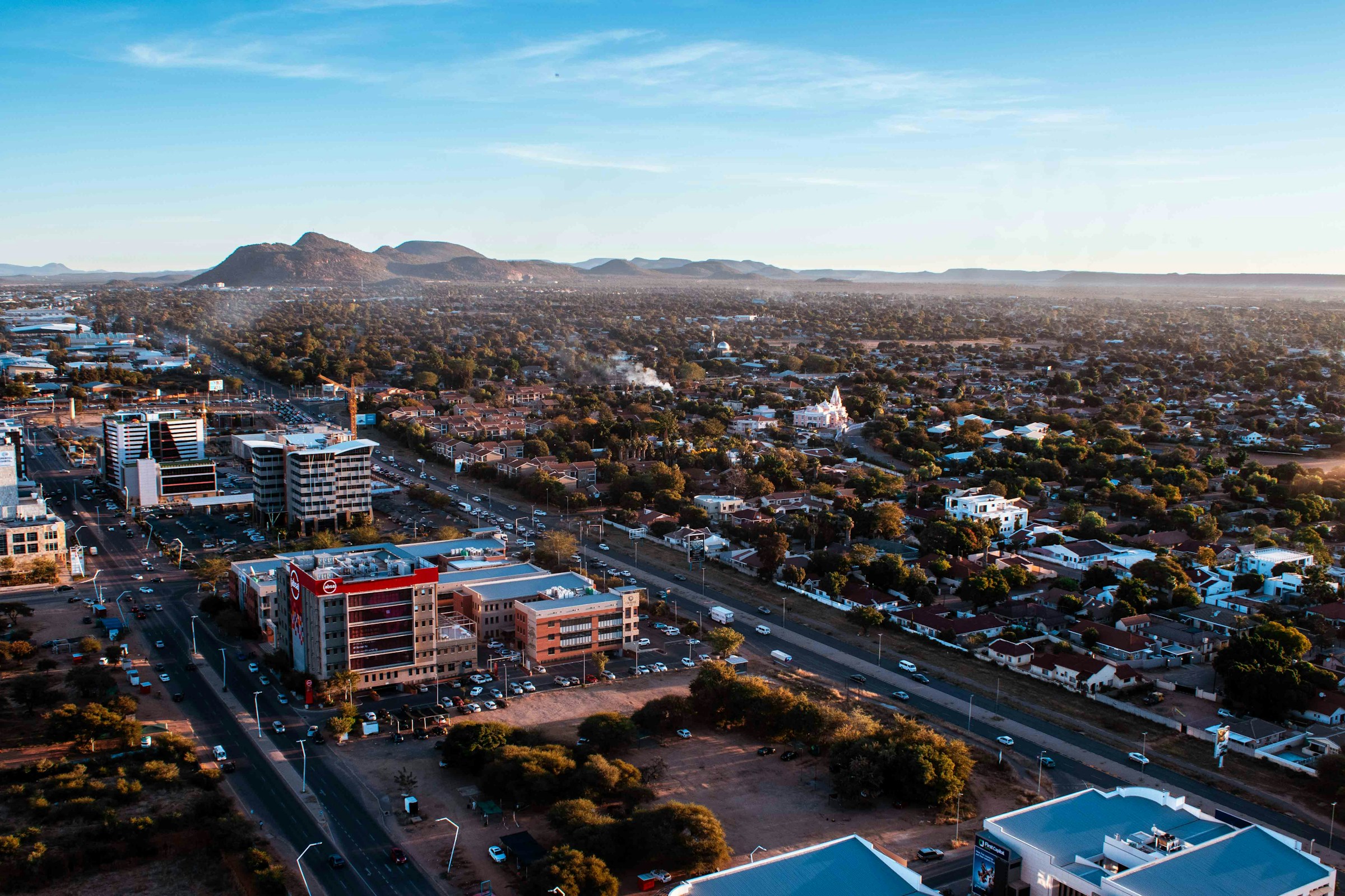Aerial view of Gaborone, Botswana showcasing urban buildings, roads, and surrounding greenery under a clear blue sky.