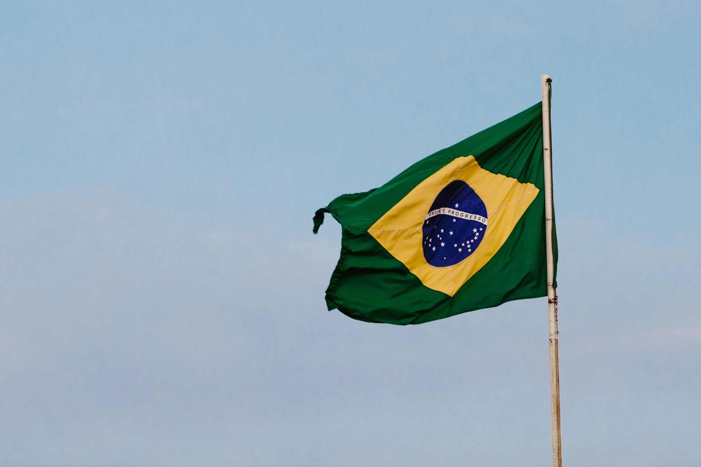 Brazilian flag waving on a pole against a clear blue sky.