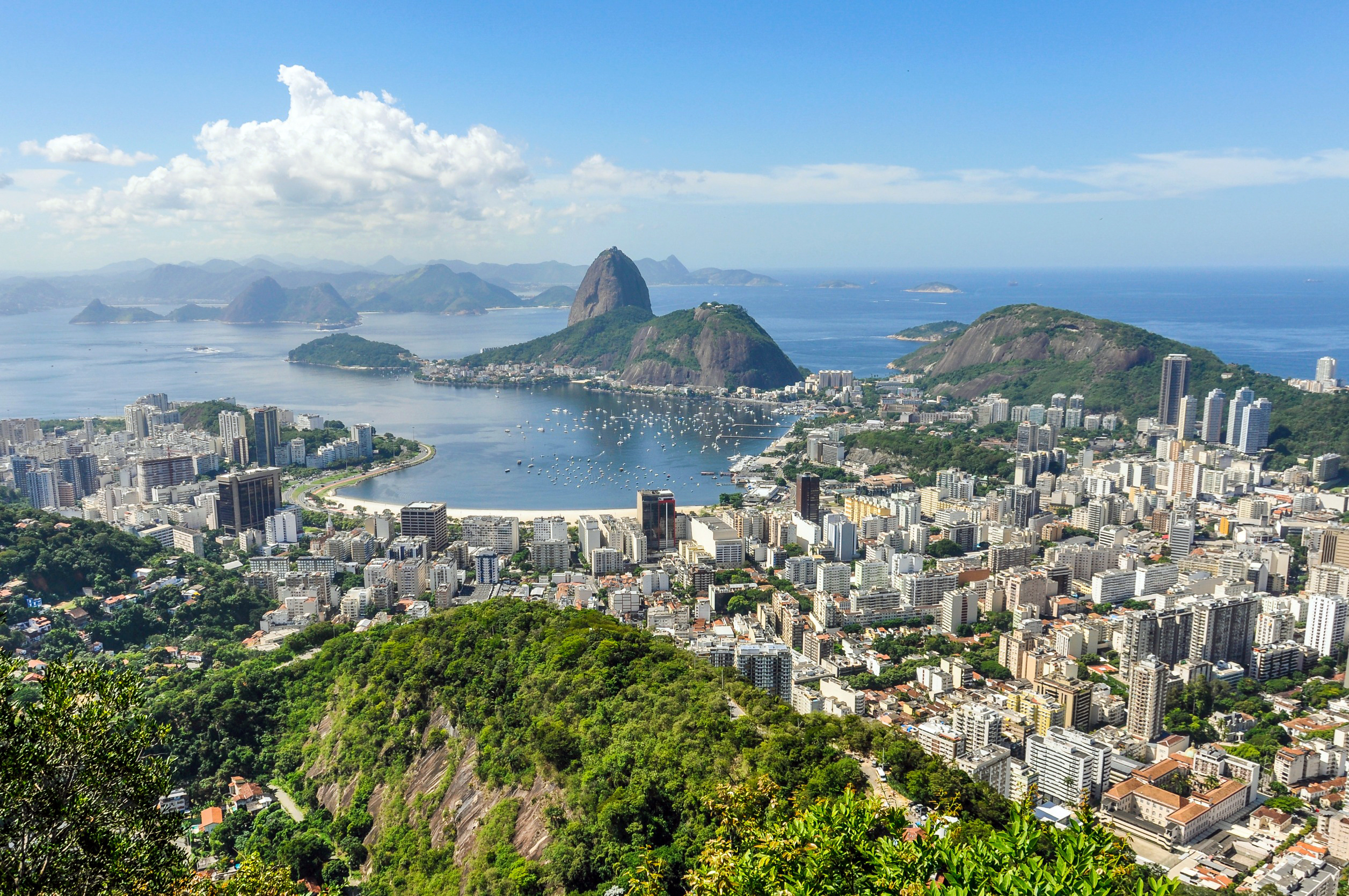 Travel to Rio de Janeiro - View featuring Sugarloaf Mountain, Guanabara Bay, and a vibrant cityscape with lush greenery under a clear blue sky.