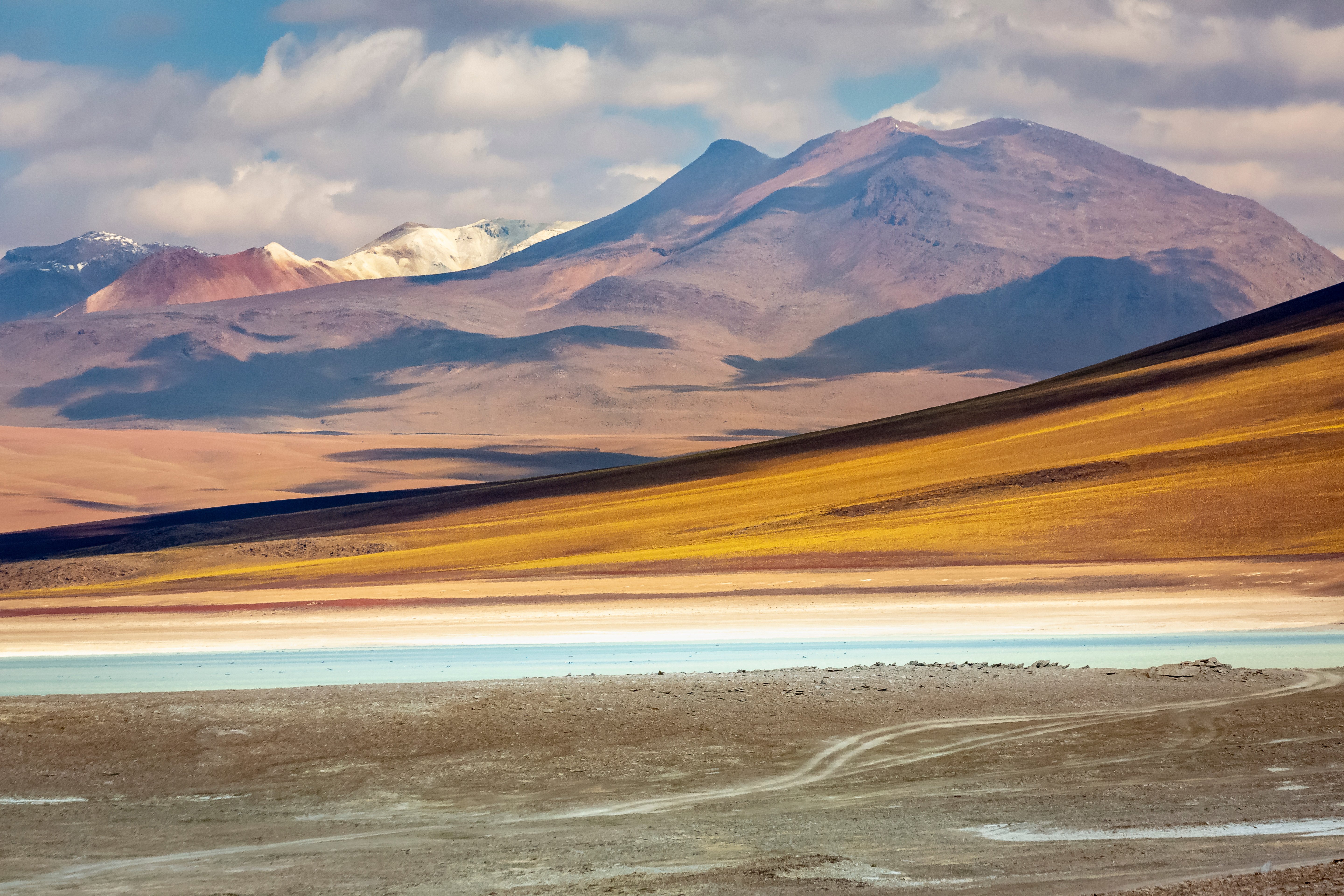 Travel to Chile - Expansive desert landscape with colorful layers, featuring rolling hills and distant mountains under a partly cloudy sky.