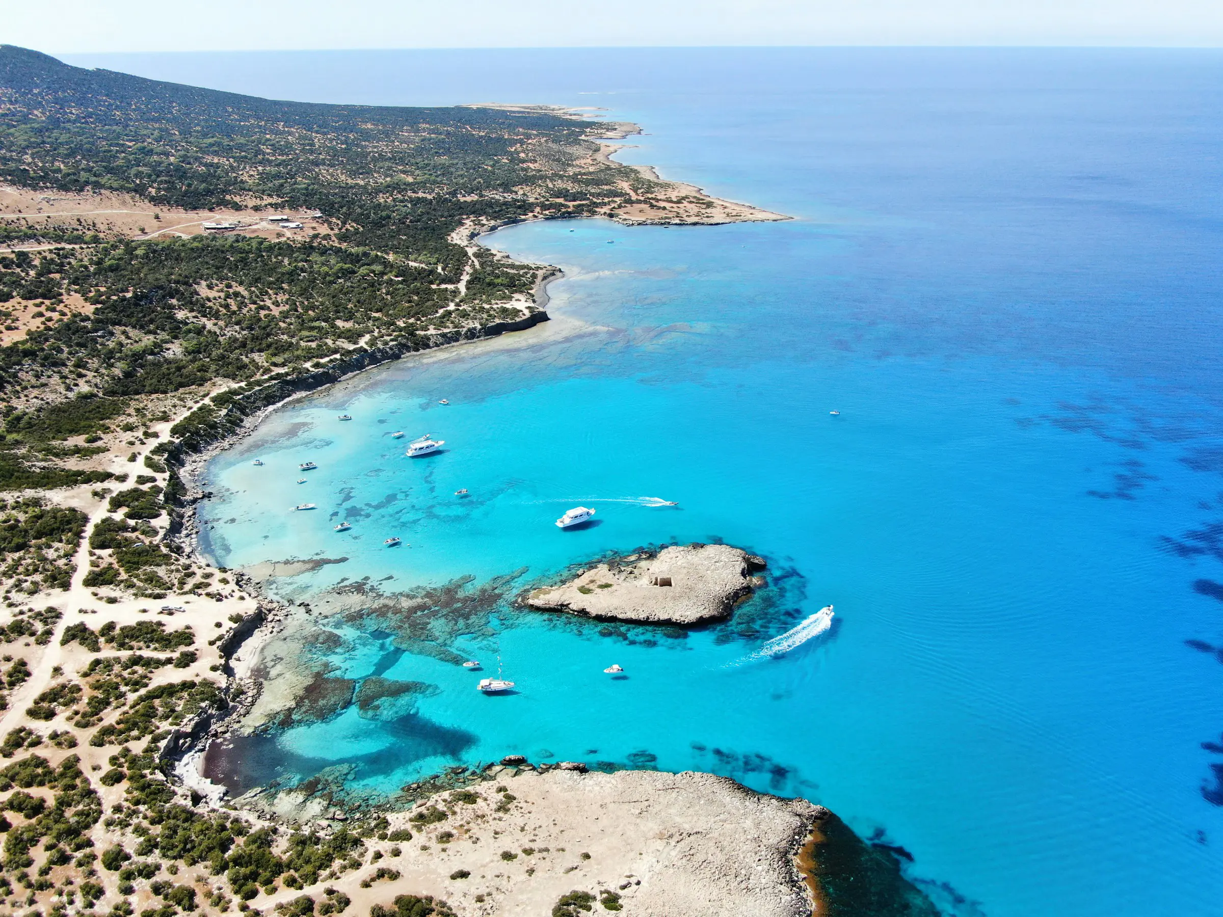 Aerial view of the Akamas Peninsula in Cyprus featuring clear turquoise waters, rocky coastline, lush greenery, and boats in the sea.