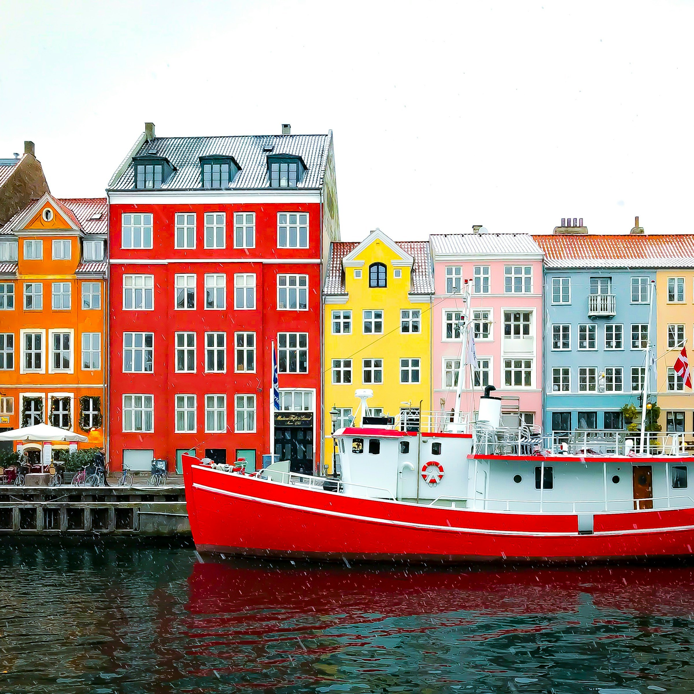 Colorful buildings line the waterfront in Nyhavn, Copenhagen, with a red boat in the foreground reflecting in the canal.