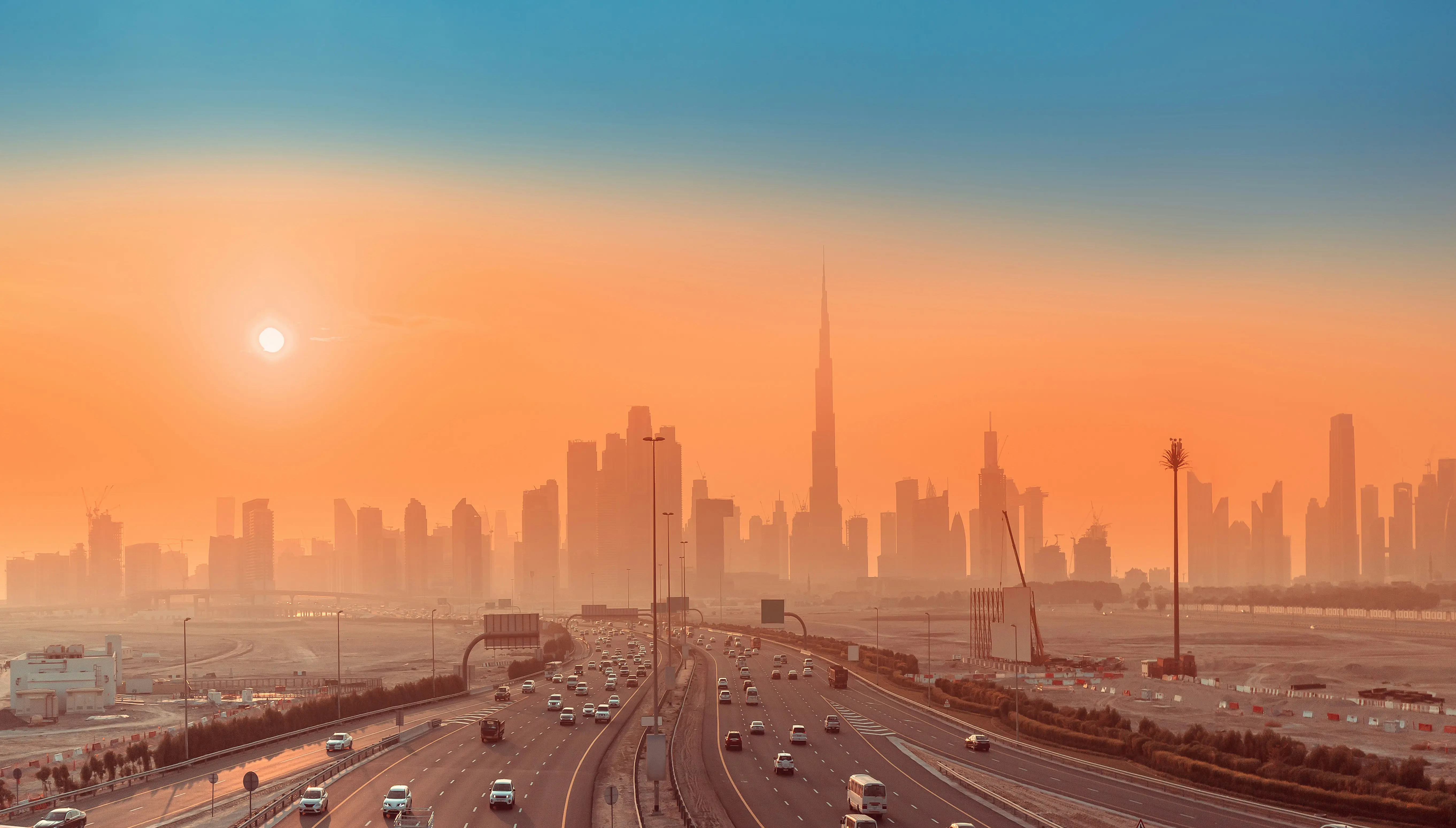 Dubain horisontti auringonlaskun aikaan, Burj Khalifa ja vilkas moottoritie etualalla, oranssia taivasta vasten
