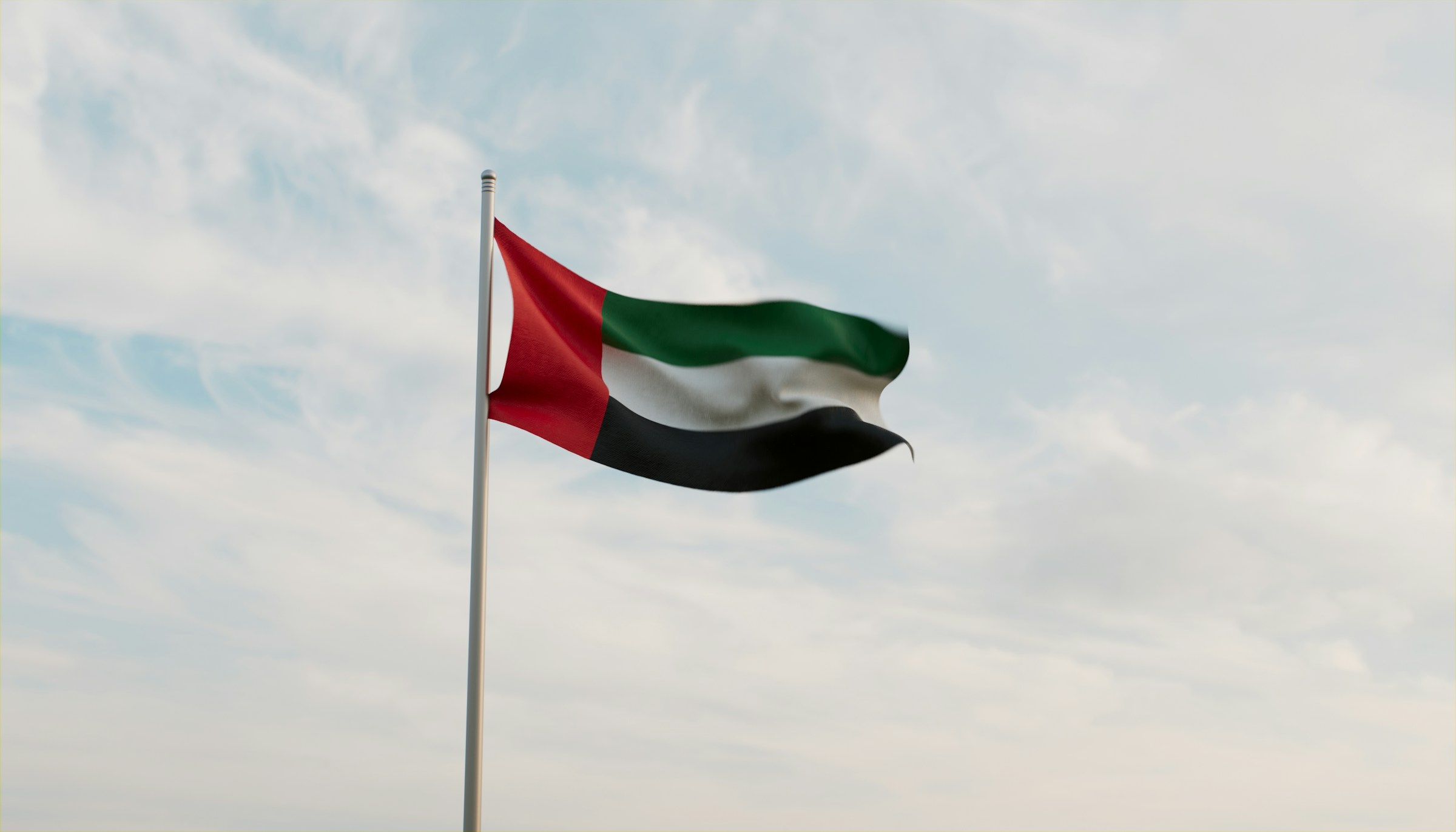United Arab Emirates flag waving on a pole against a cloudy sky background.