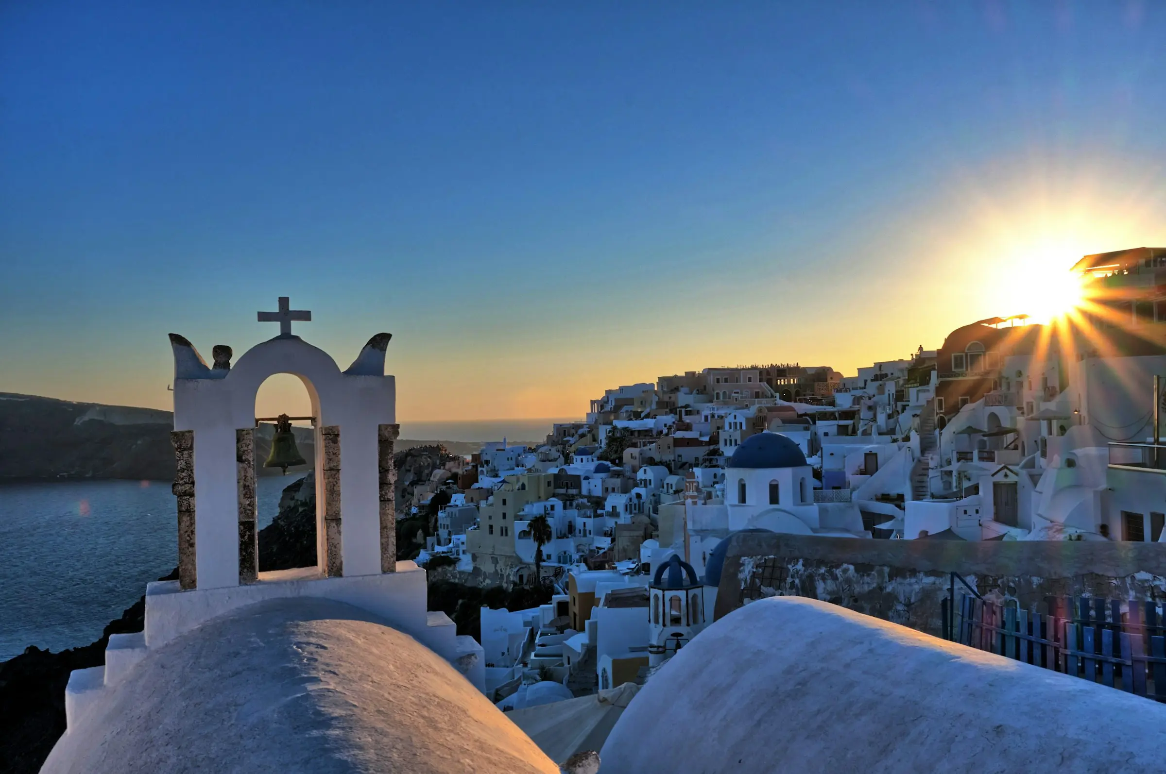 Solnedgång över Santorini med traditionella vita byggnader och blå kupoler i förgrunden