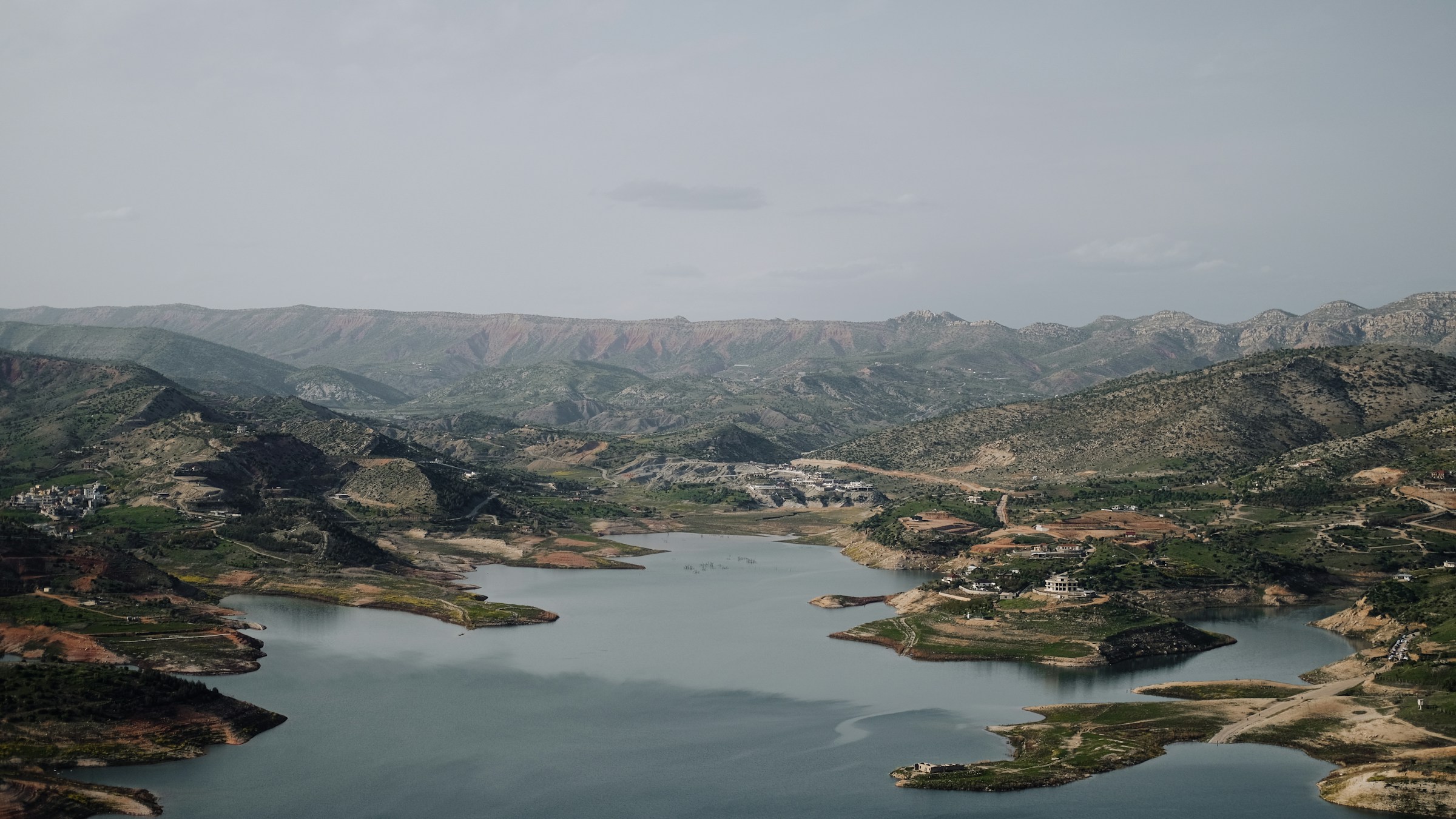 Mountainous landscape with a winding river, featuring lush greenery and scattered settlements under an overcast sky.