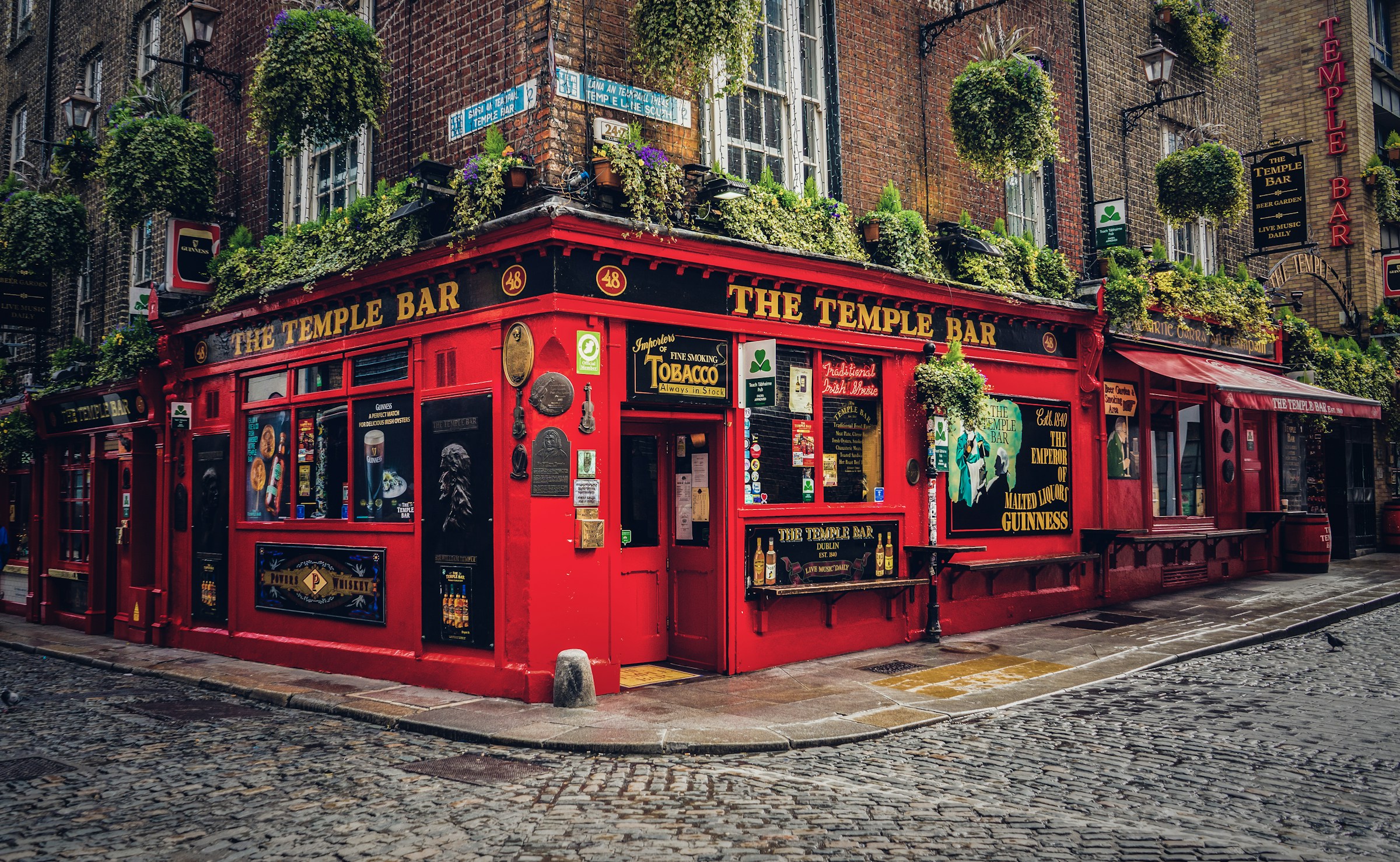 Historic Temple Bar pub in Dublin, Ireland, featuring red exterior with signs and flower planters along a cobblestone street.