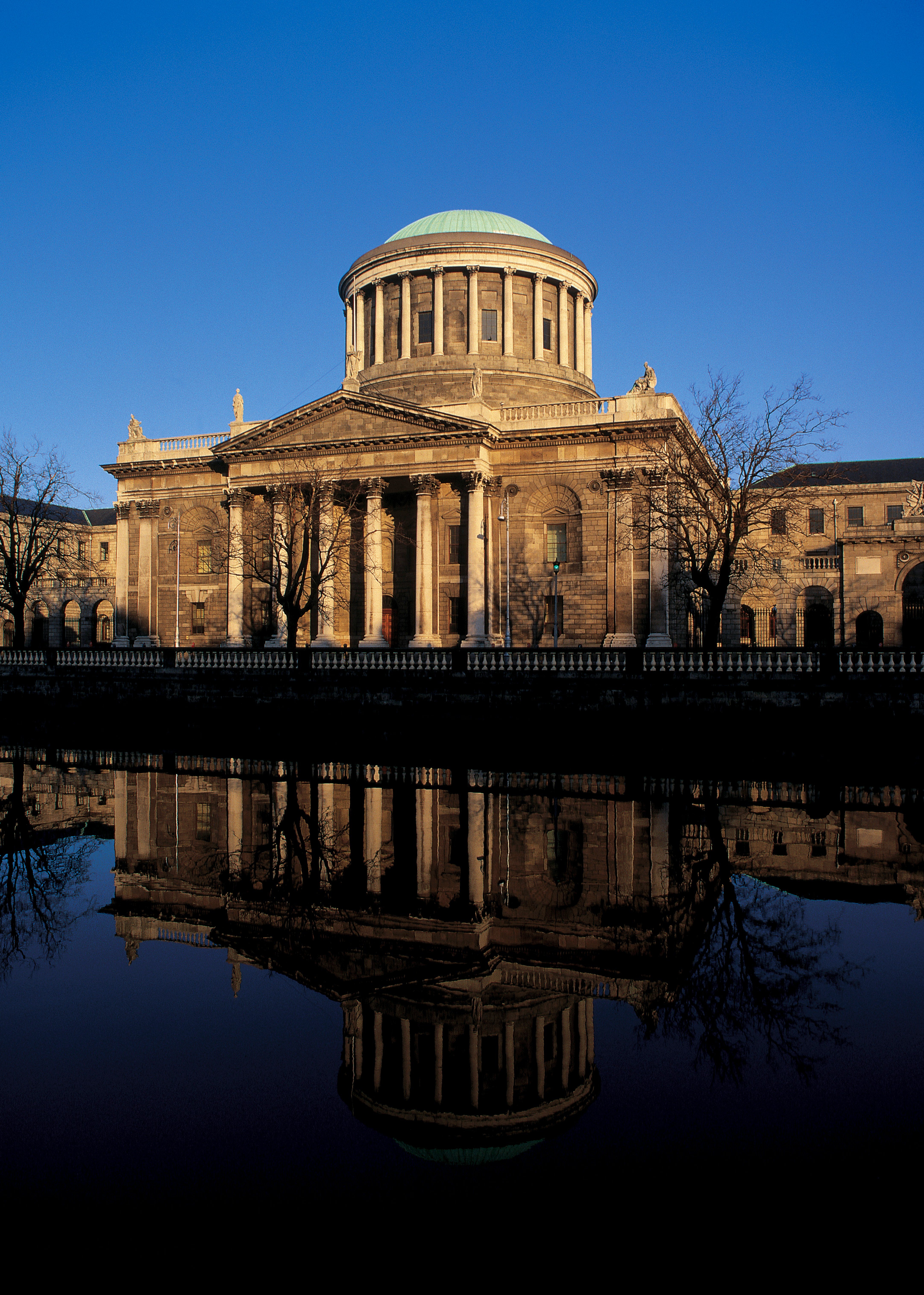 Historisk byggnad med kupol och kolonner reflekteras i vattnet, mot en klar blå himmel