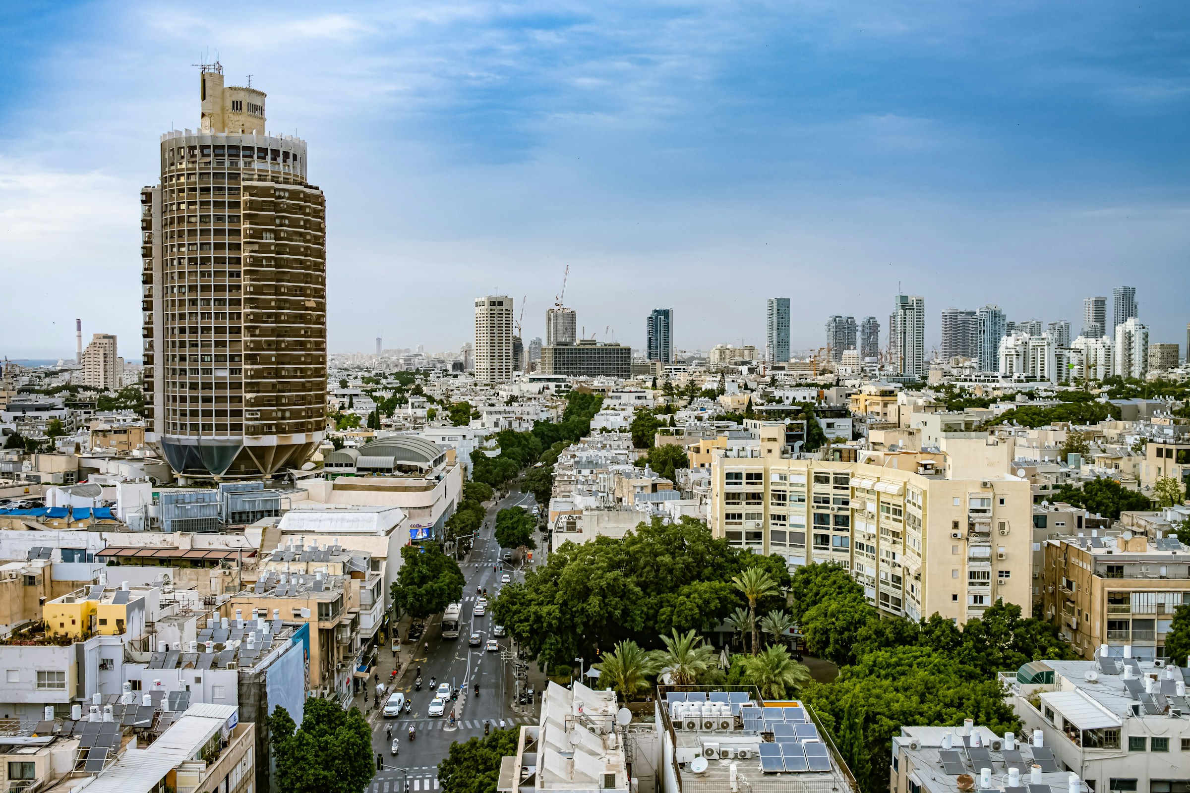 Panoramic view of Tel Aviv cityscape, featuring iconic circular skyscraper and modern high-rises under a cloudy sky.