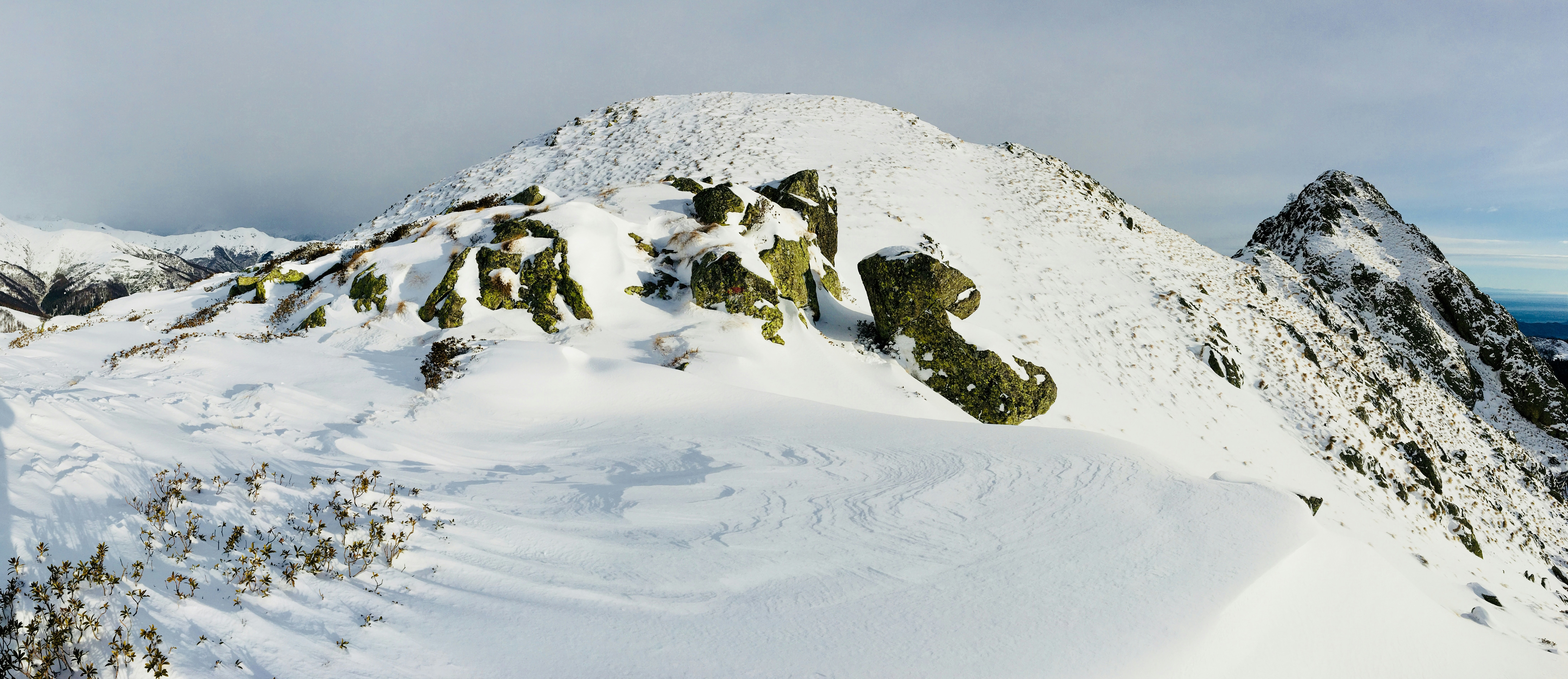 Snötäckt bergstopp med mossiga klippor under en molnig himmel i Alagna, Italien.