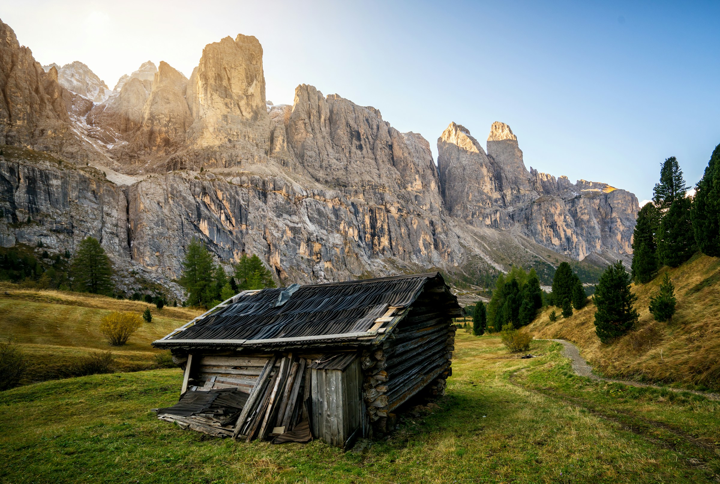 Yksinäinen mökki seisoo vihreässä laaksossa mahtavien kallioiden välissä Val Gardenassa auringonnousun taustalla
