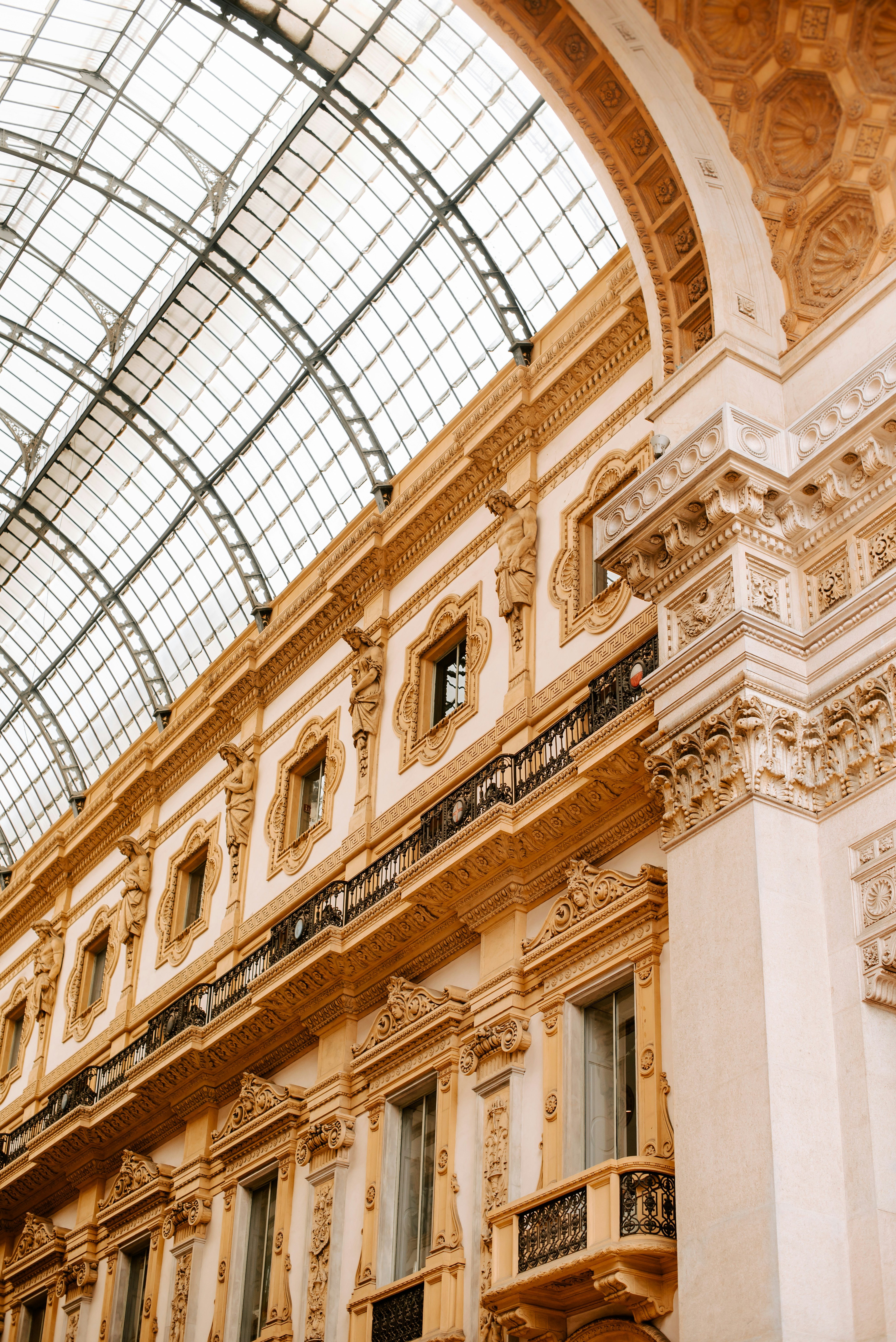 Interior view of an ornate 19th-century shopping arcade with a glass dome ceiling and detailed architectural features, including decorative moldings and statues.