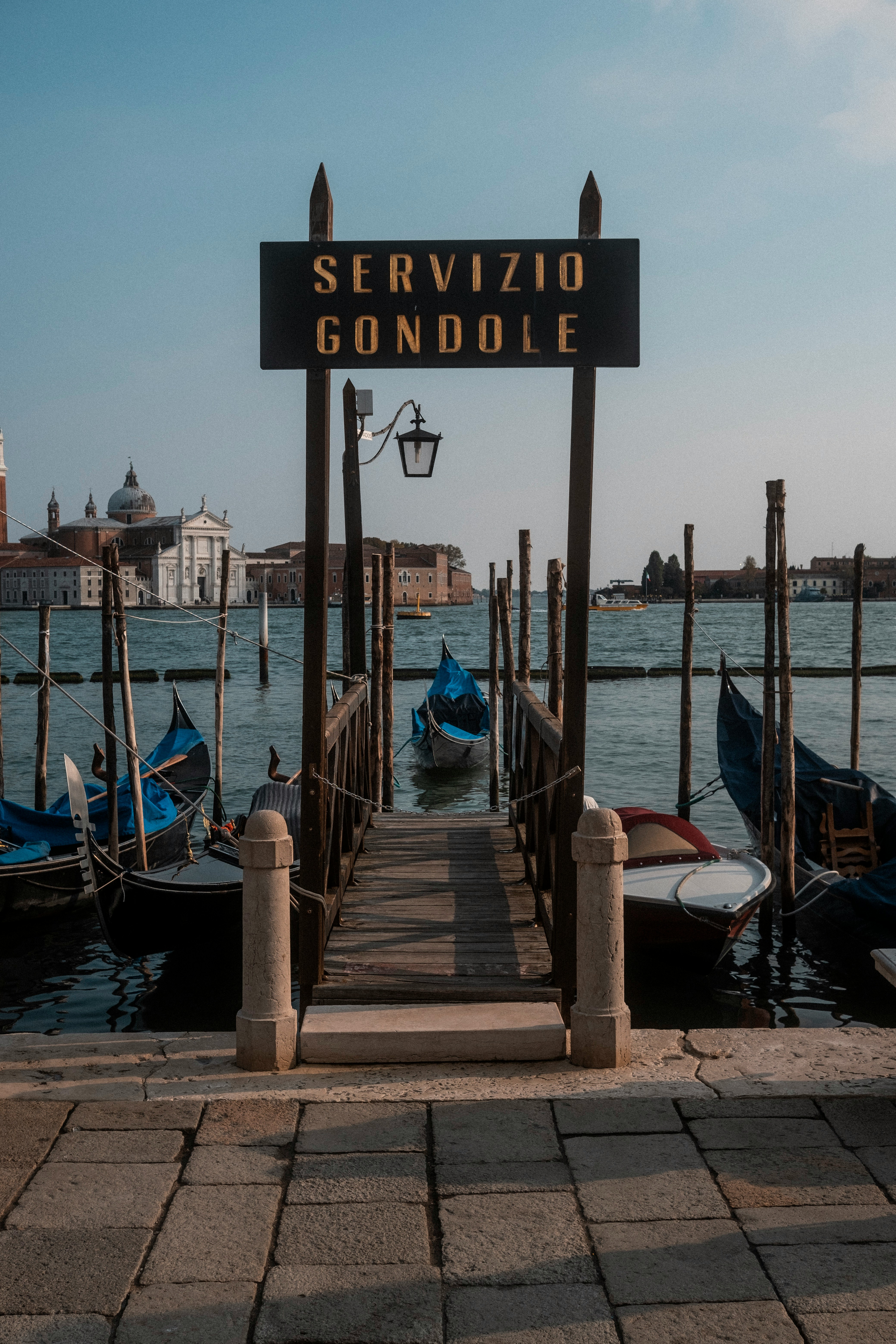 Gondolilaituri Venetsiassa, jossa on opaste "Servizio Gondole", taustalla historiallisia rakennuksia ja kanaali