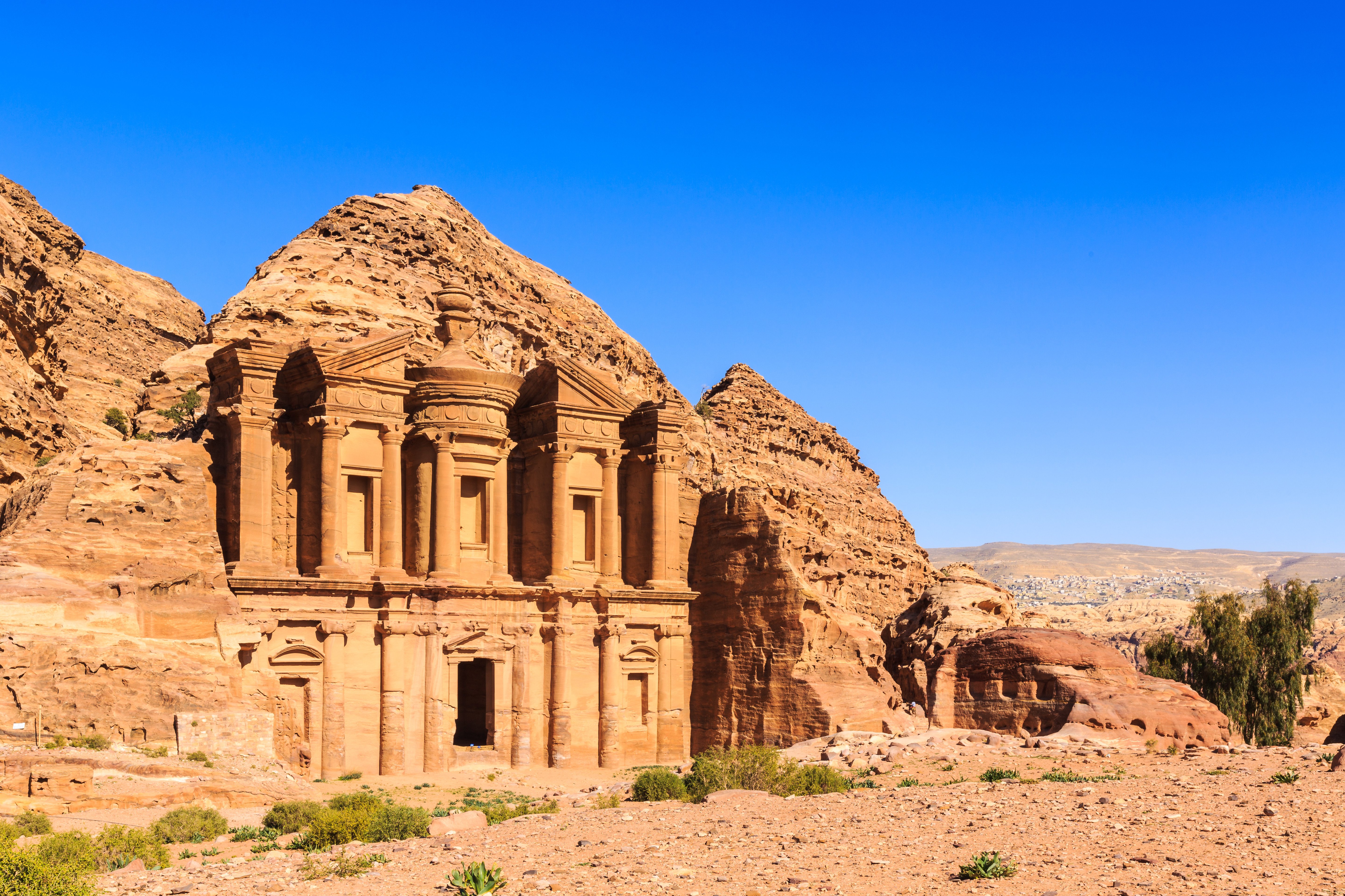 Historiska klippstaden Petra i Jordanien under klar blå himmel, featuring det ikoniska El Deir-klostret hugget i sandsten