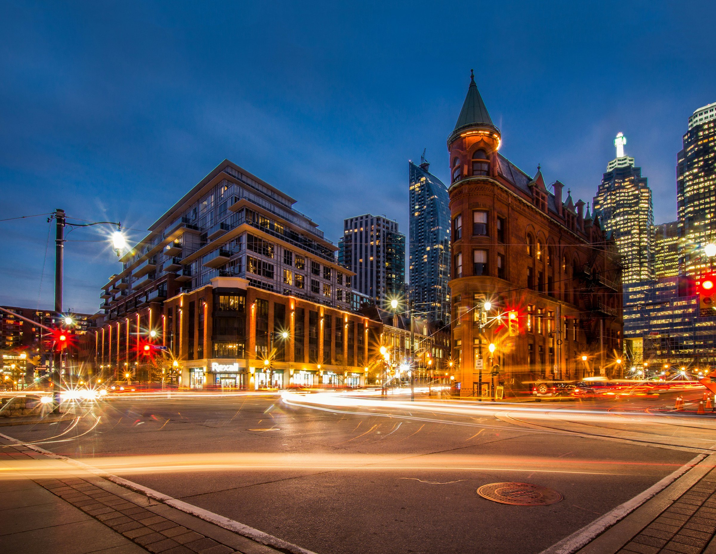 City street at night with light trails from traffic, featuring historic buildings and modern skyscrapers against a twilight sky.