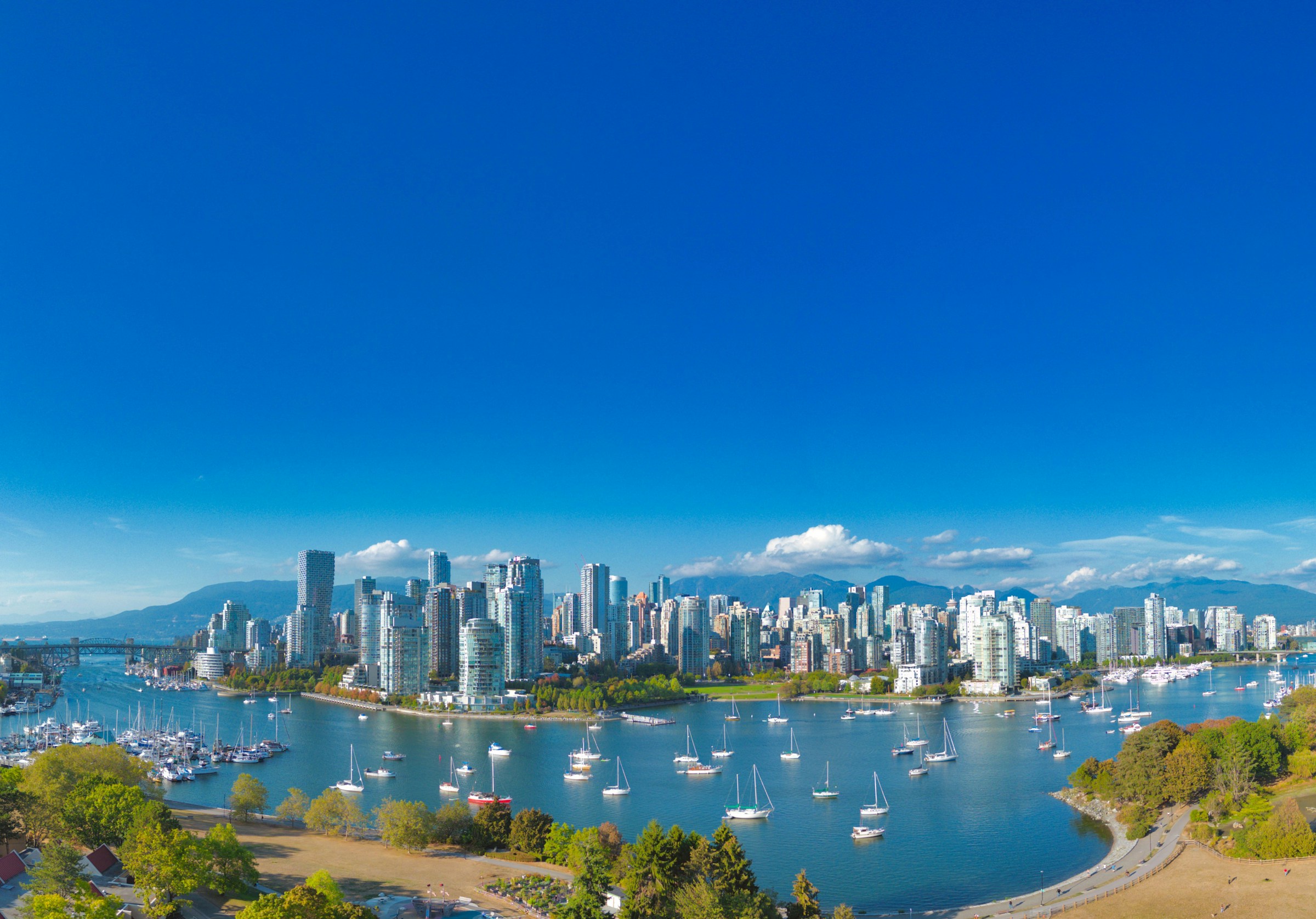 Vancouver skyline with modern skyscrapers and boats in the harbor, under a clear blue sky.