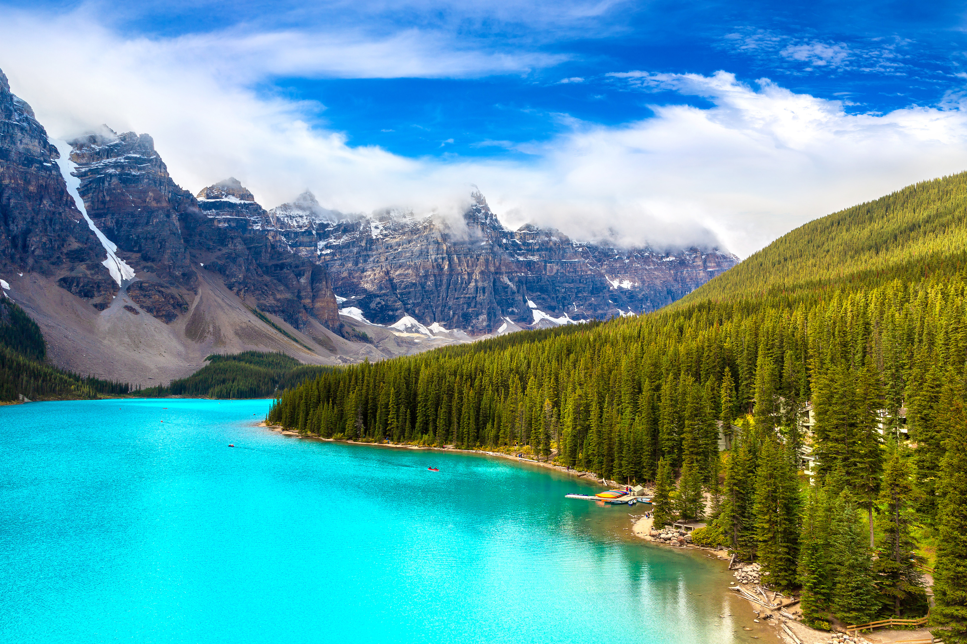 Turkosblått vatten i Moraine Lake omgiven av gröna tallar och majestätiska berg i Banff National Park, Kanada, under en klarblå himmel
