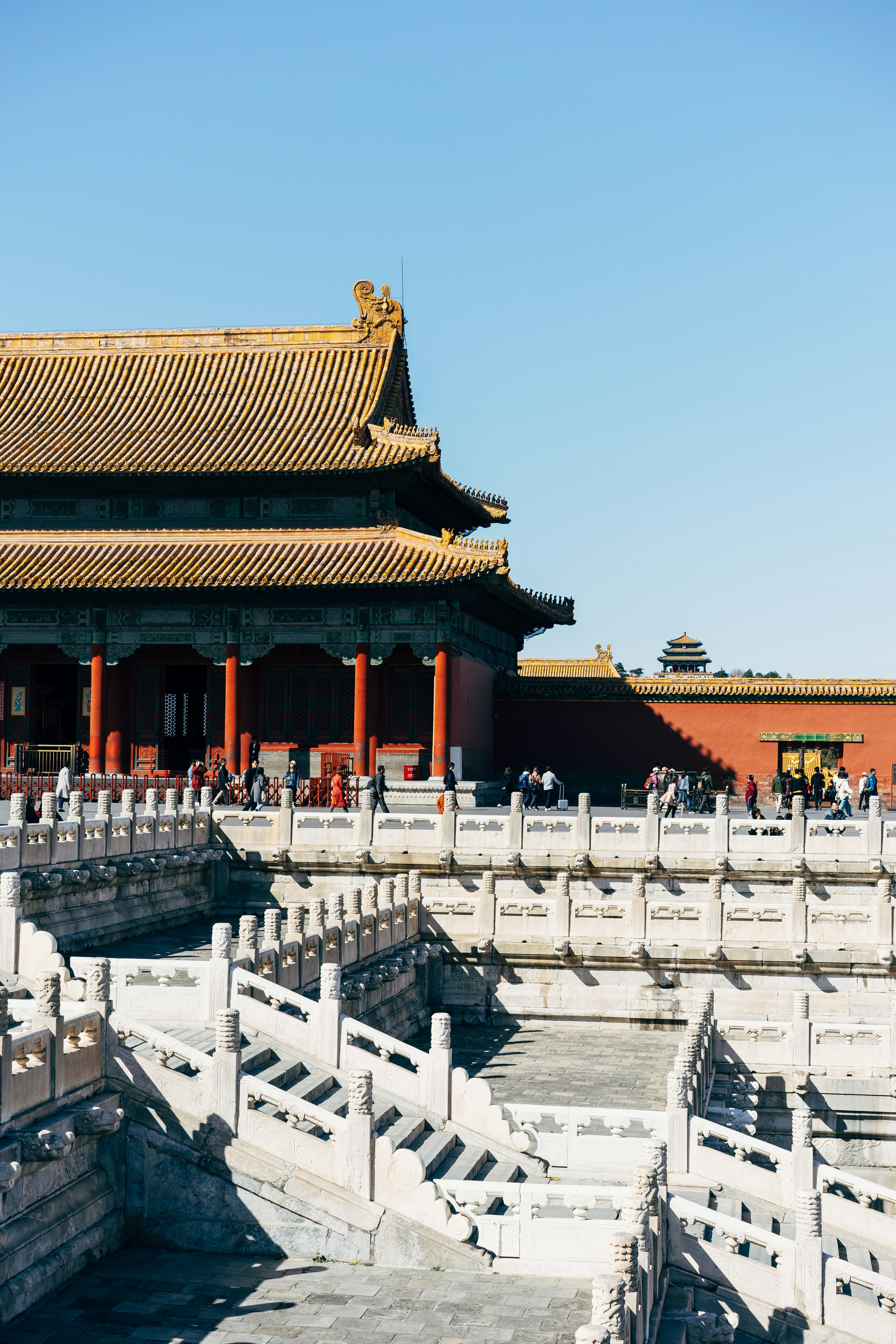 Antik träbyggnad med traditionell kinesisk arkitektur i Den förbjudna staden, Peking, med utsmyckade stenräcken och en klarblå himmel