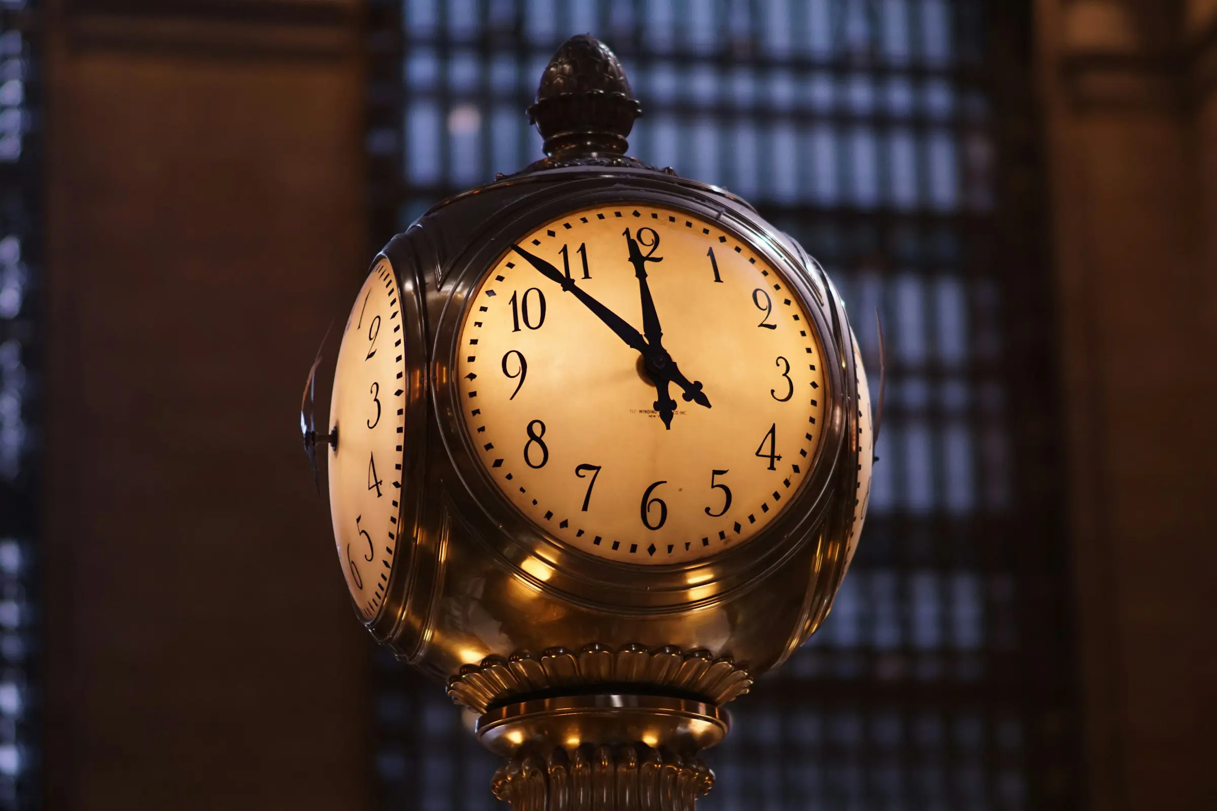 Ornamenterad klocka inuti Grand Central Terminal som visar tiden 10:10, med en svagt upplyst, arkitektonisk bakgrund