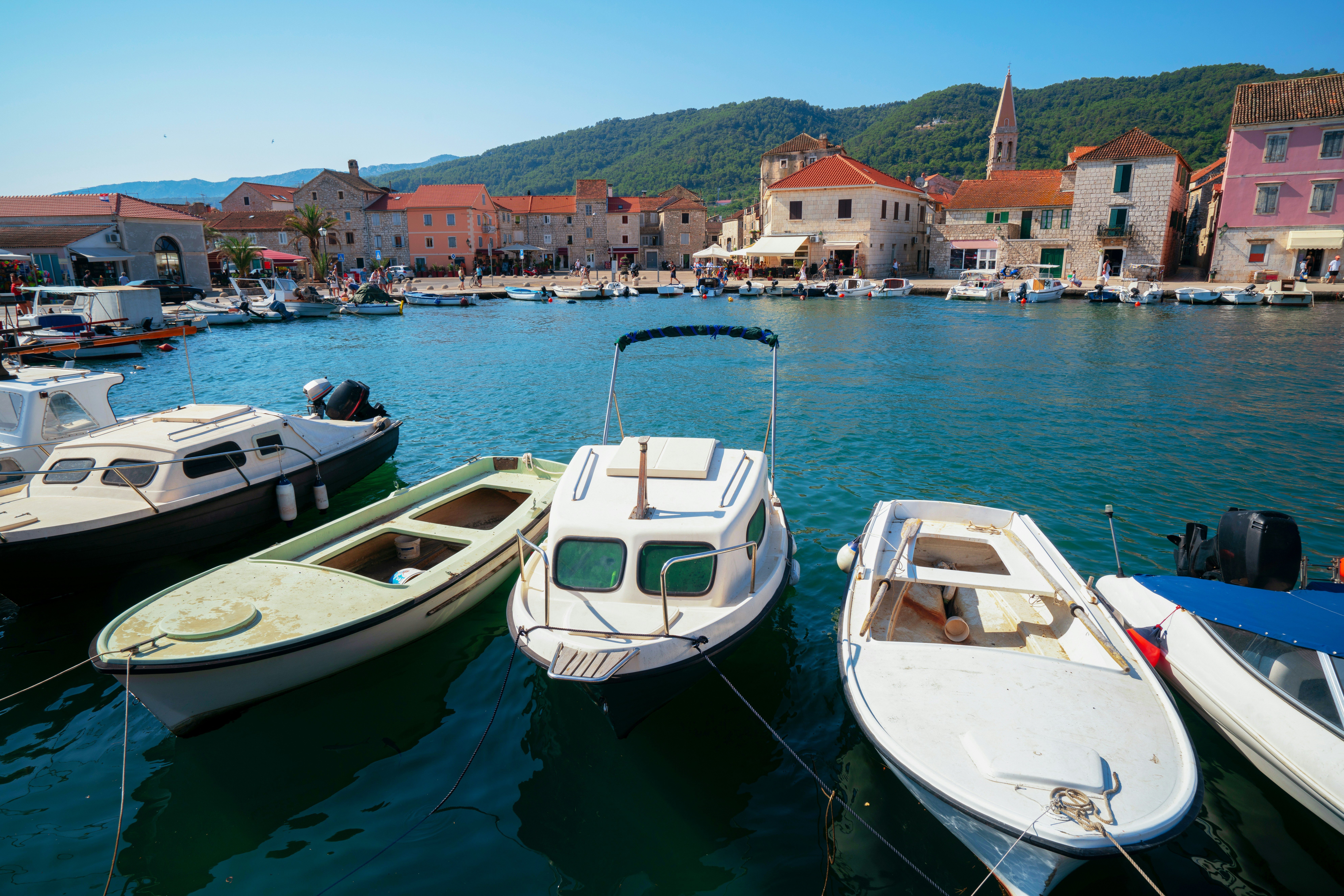 Row of small boats docked in a picturesque harbor with charming, historic buildings and lush green hills in the background