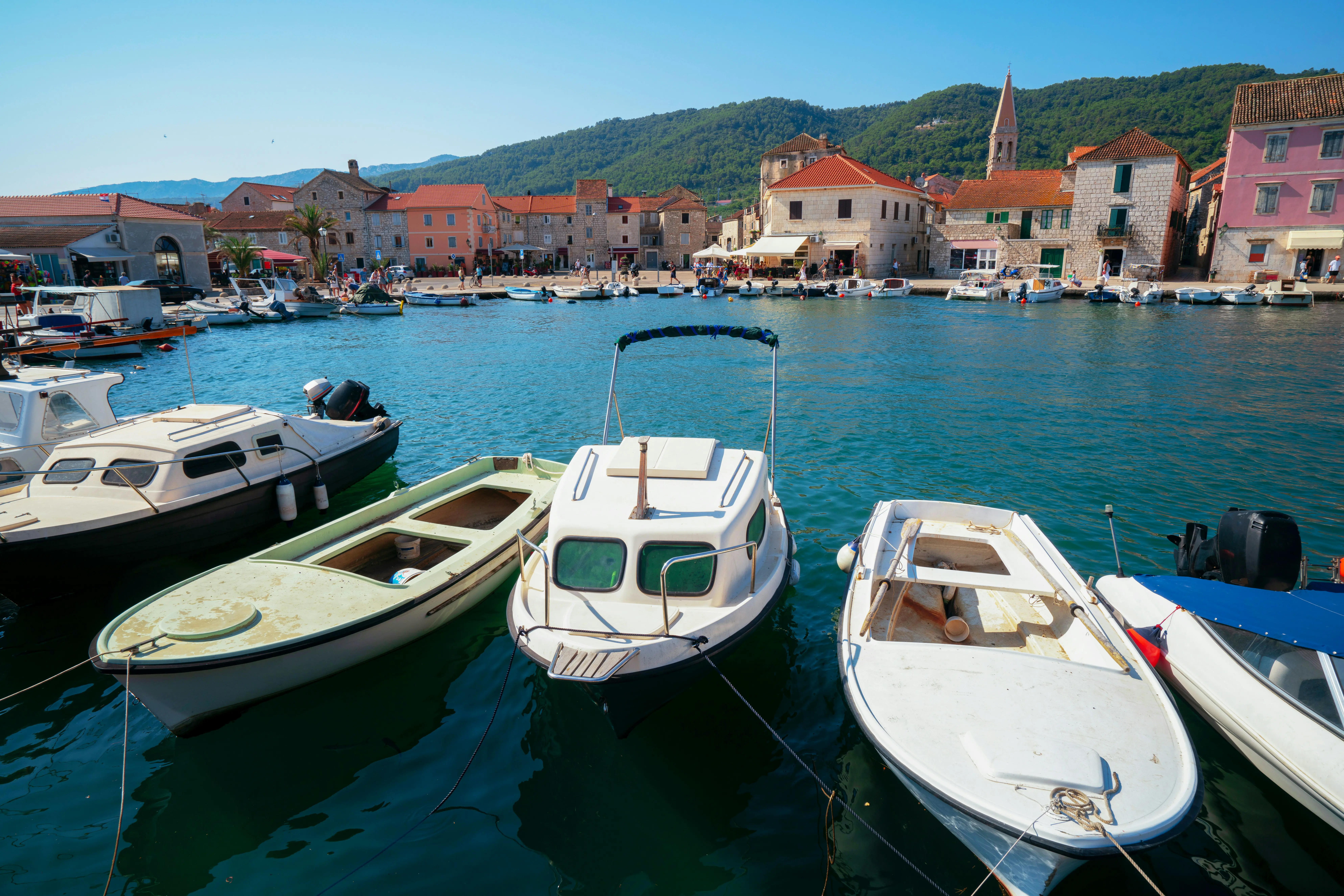 Row of small boats docked in a picturesque harbor with charming, historic buildings and lush green hills in the background