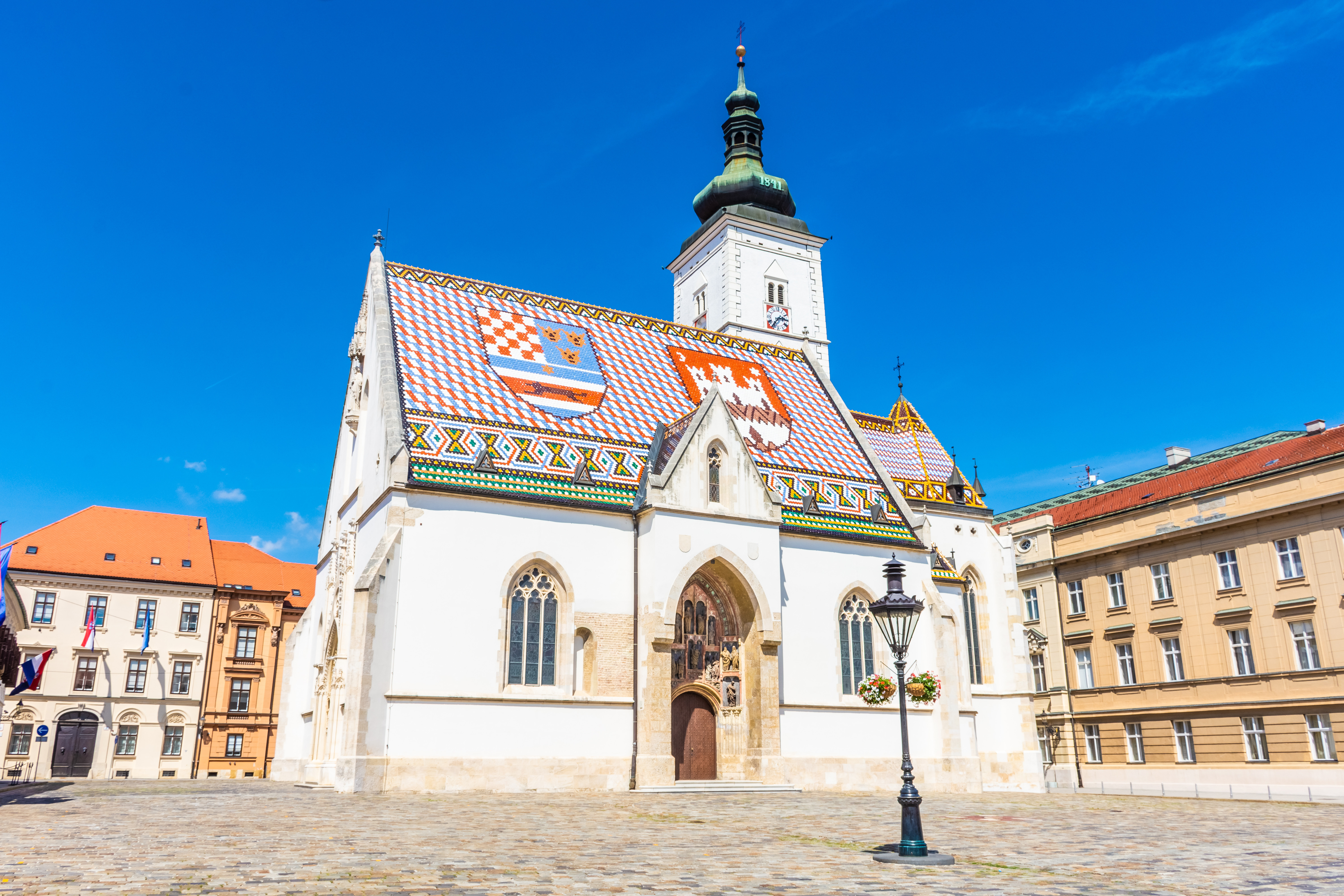 Travel to Zagreb - St. Mark's Church in Zagreb, Croatia, featuring a distinctive colorful tiled roof with city emblems and a clock tower.