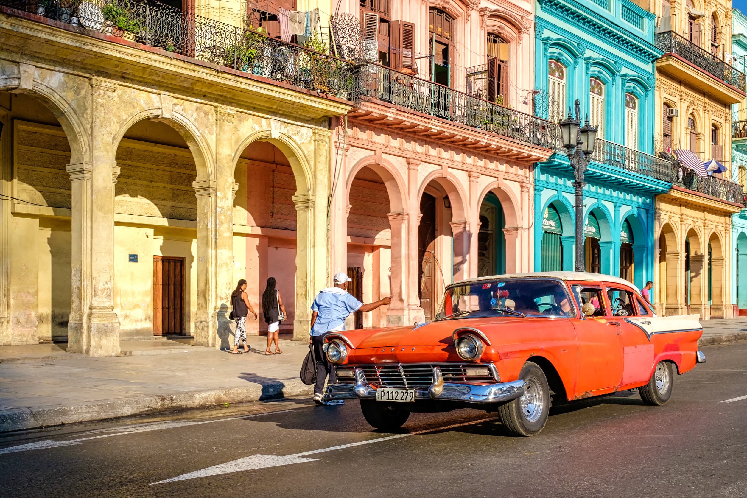 Vintage orange car driving past colorful colonial buildings in Havana, Cuba
