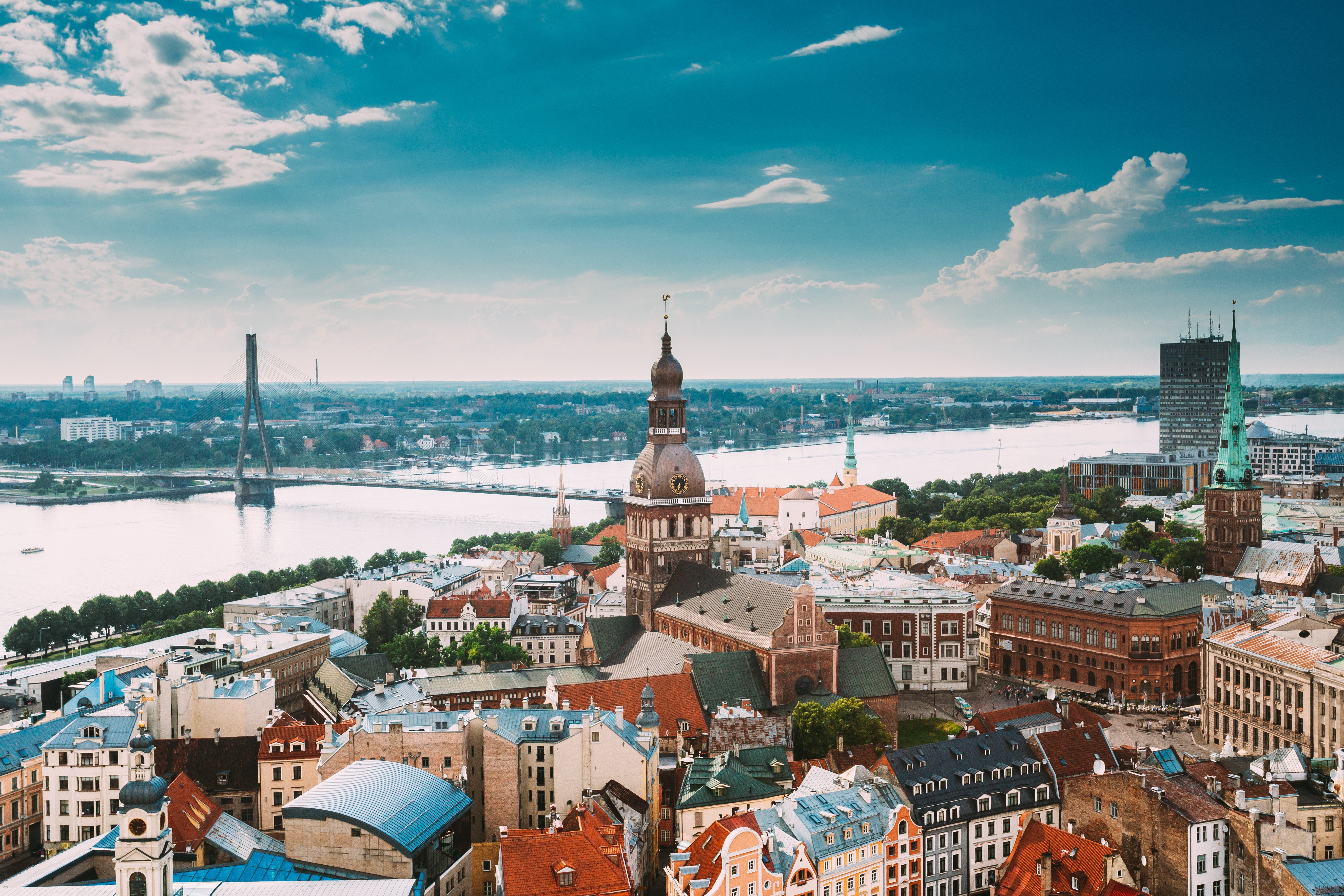 Aerial view of Riga, Latvia, featuring historic architecture, the Daugava River, and modern buildings under a blue sky