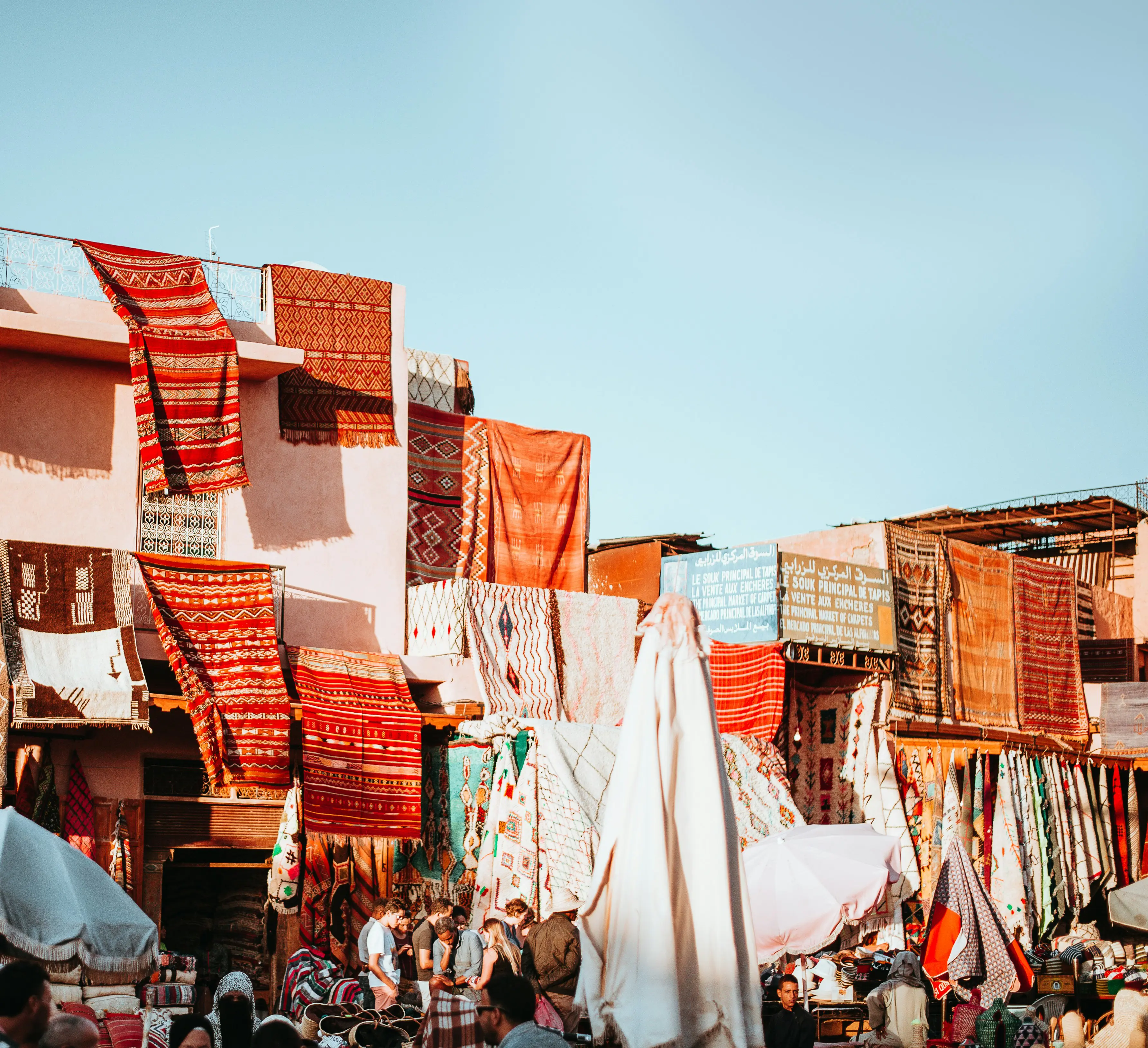 Colorful Moroccan rugs hanging on the walls of a market in Marrakech, showcasing intricate patterns and vibrant hues under a clear blue sky